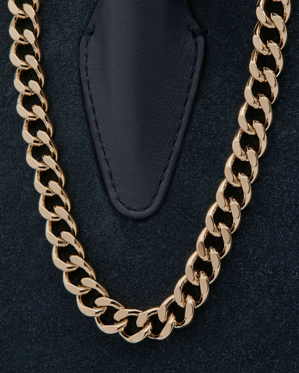 Navy suede mini tote showing gold chain strap and stitched leather tab.