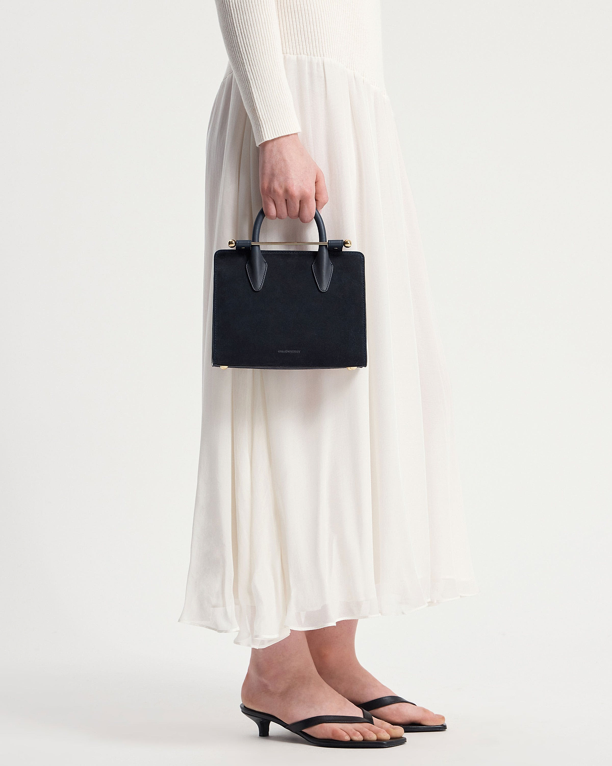Model's lower body holding a navy suede mini tote with a gold bar handle.