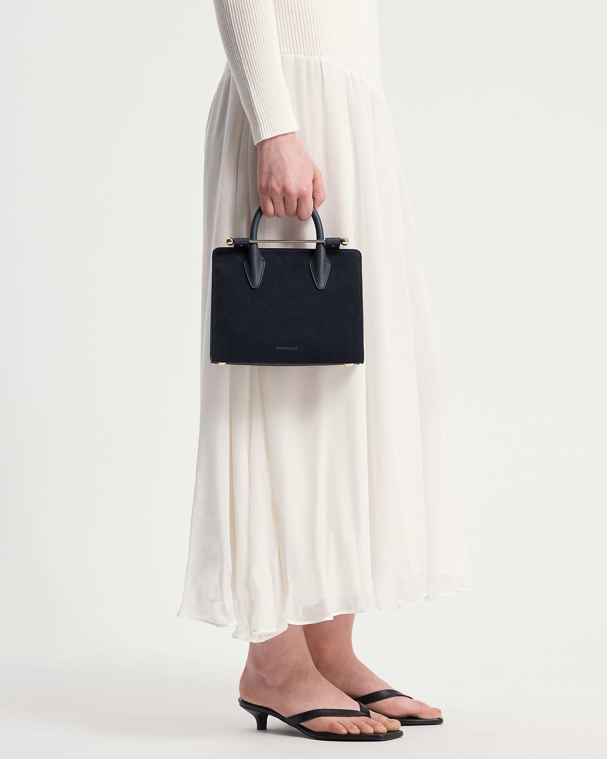 Model's lower body holding a navy suede mini tote with a gold bar handle.