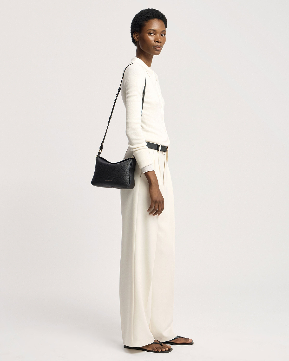 Model in white outfit carrying black Strathberry Sway shoulder bag