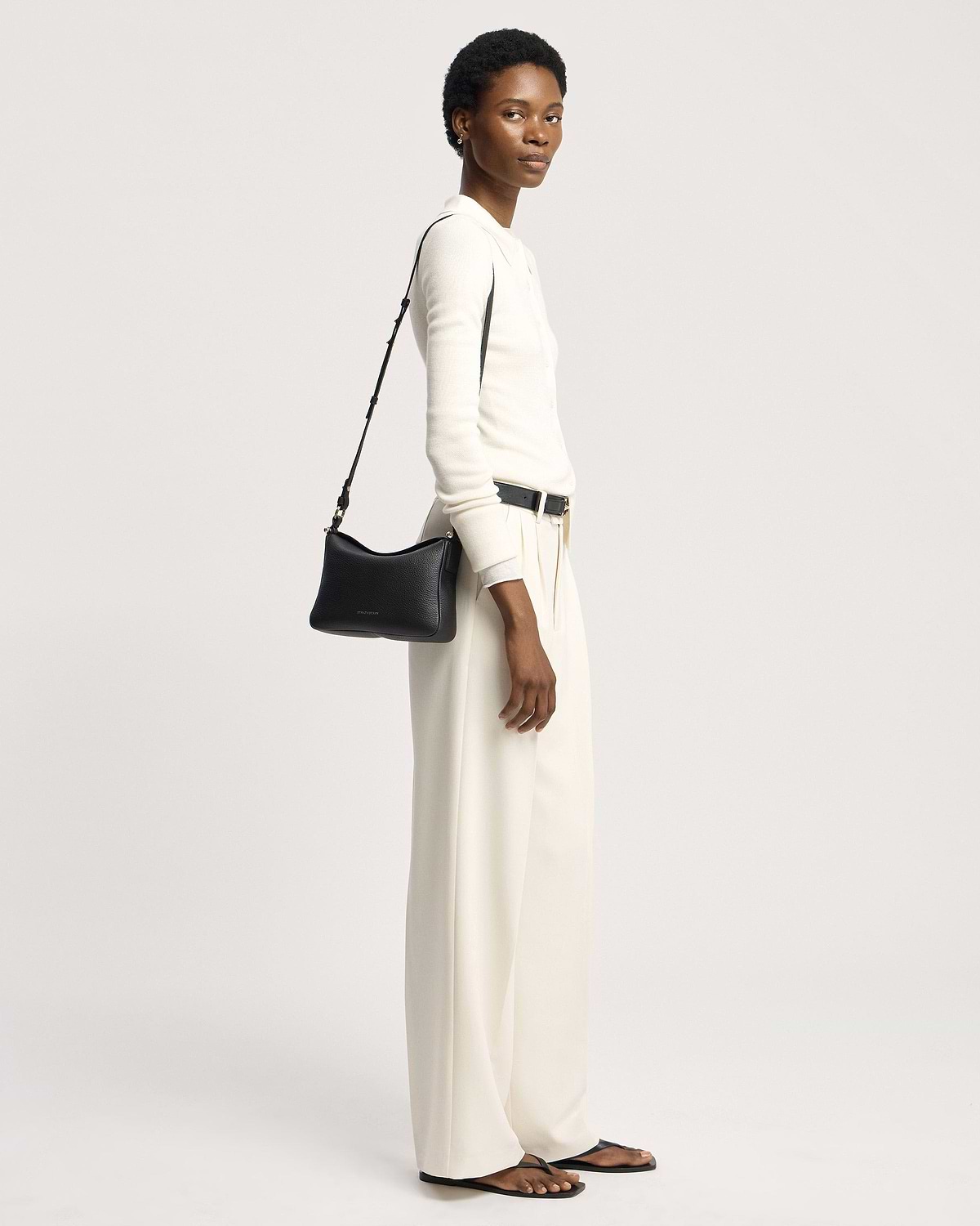 Model in white outfit carrying black Strathberry Sway shoulder bag