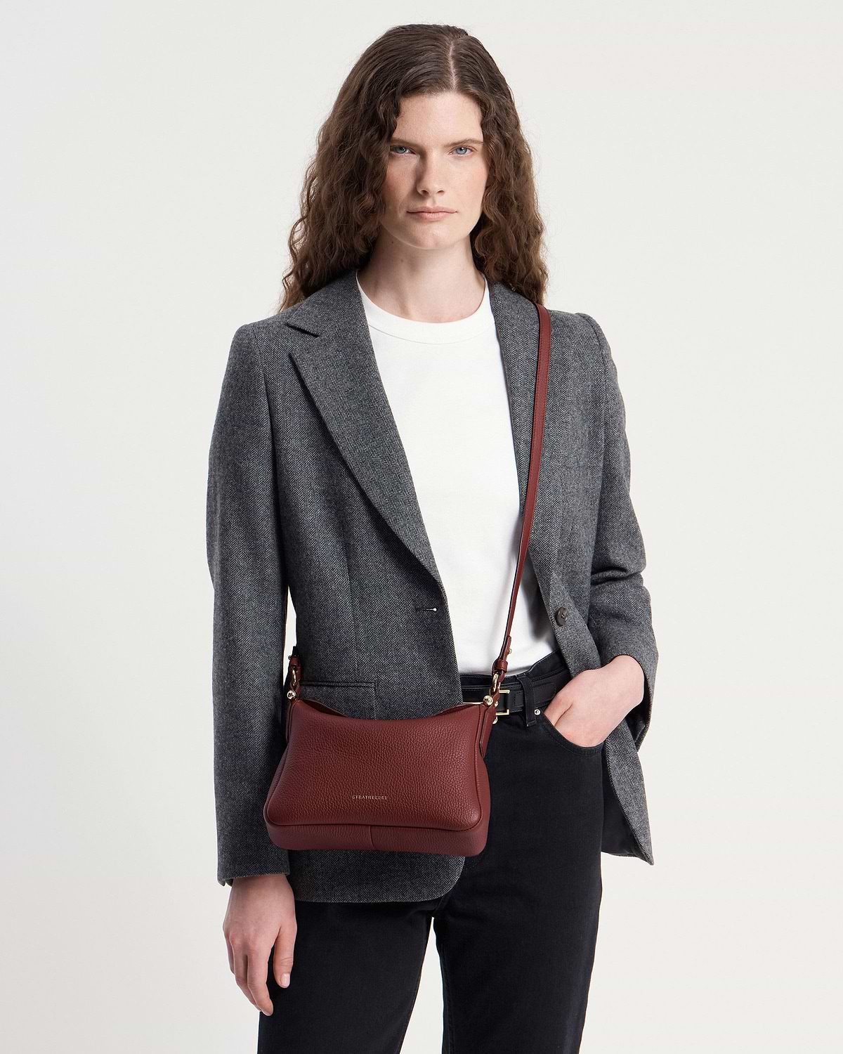 Model wearing a grey blazer and white t-shirt with oxblood Strathberry Sway bag.