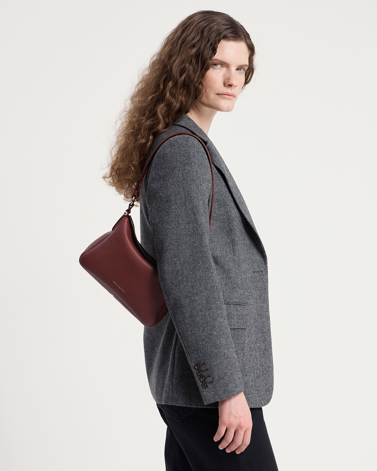 Model in grey blazer carrying an oxblood Sway shoulder bag.