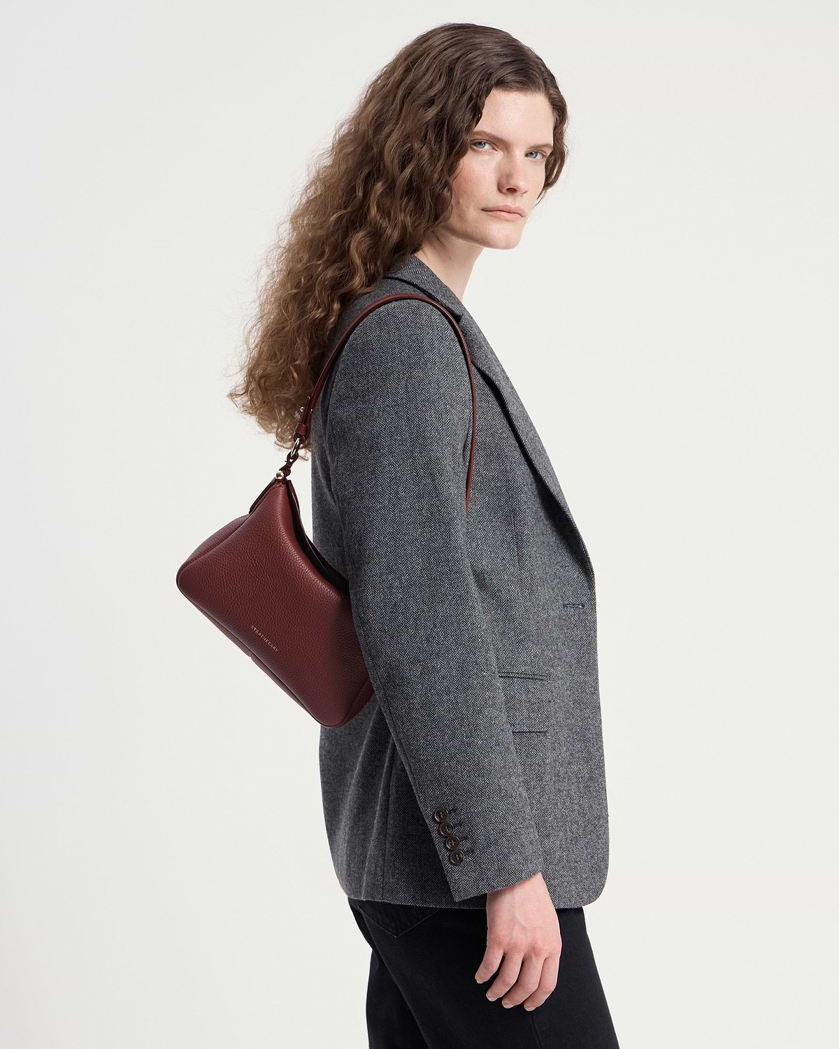 Model in grey blazer carrying an oxblood Sway shoulder bag.