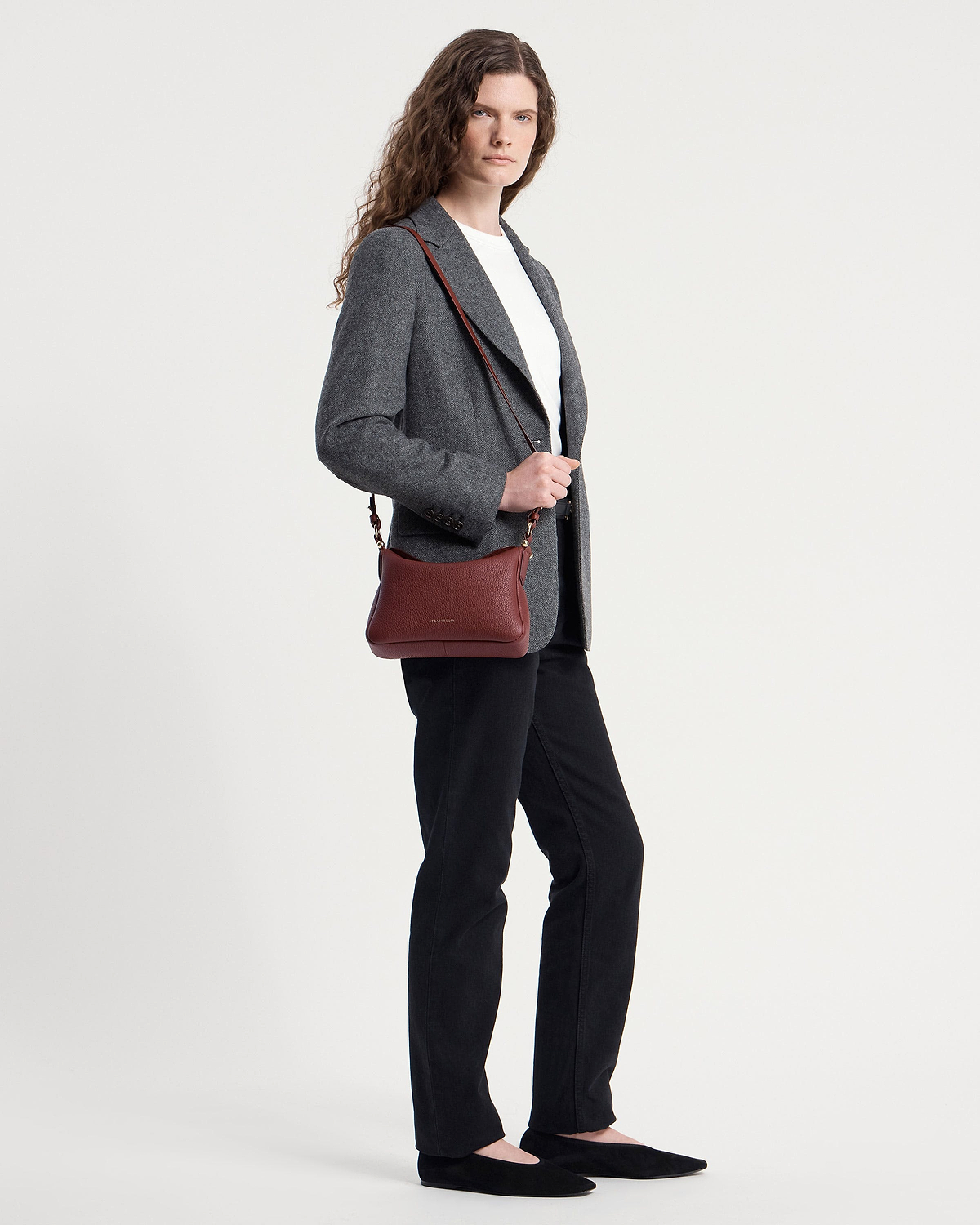 Model wearing an oxblood Sway shoulder bag across the body with a grey blazer.