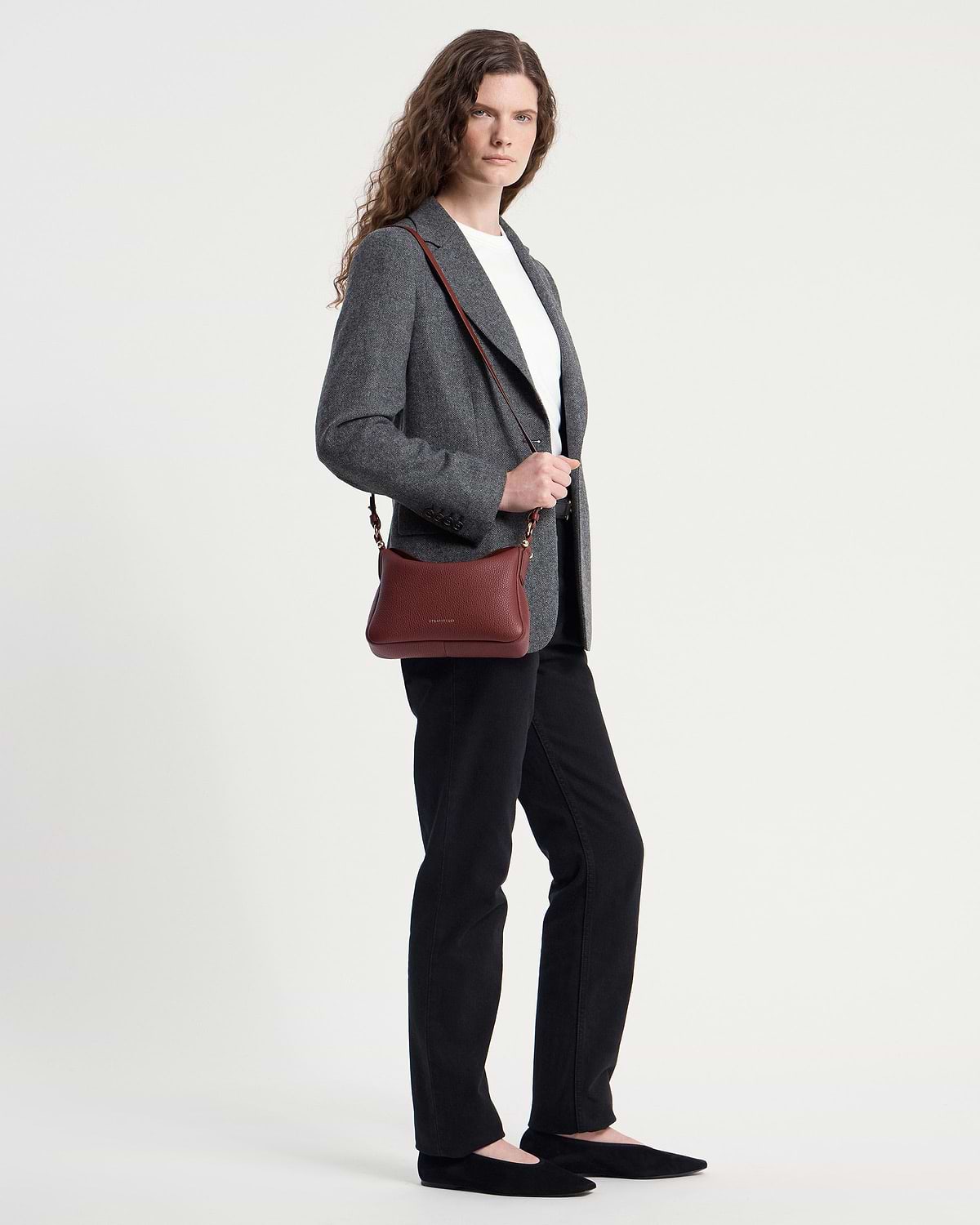 Model wearing an oxblood Sway shoulder bag across the body with a grey blazer.