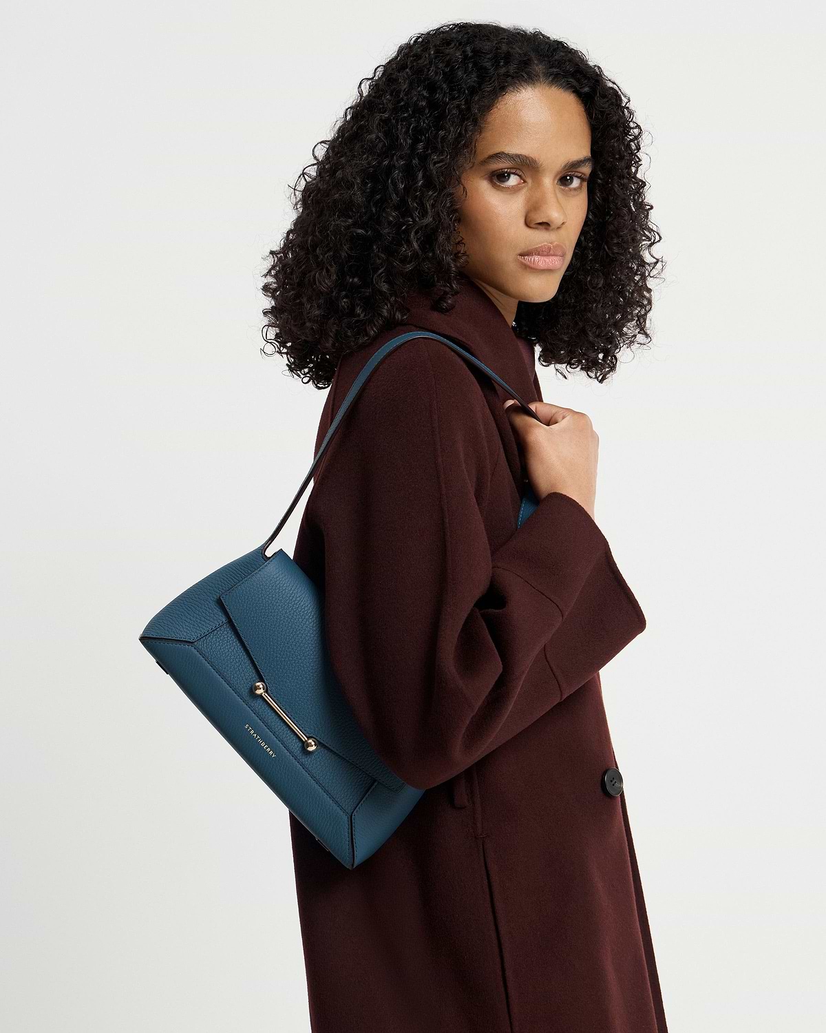 Model wearing burgundy coat holding Strathberry Mosaic Shoulder bag in Loch Blue