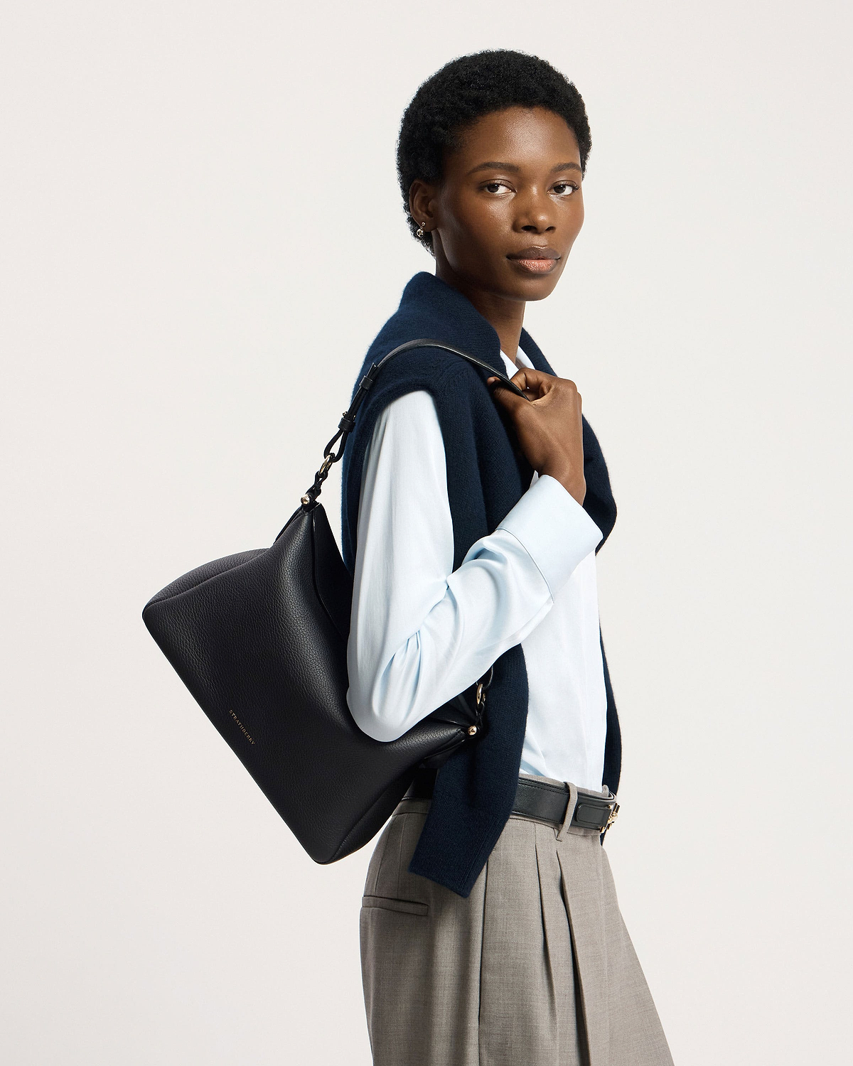 Model carrying black Strathberry Sway Maxi shoulder bag, wearing blue shirt and navy sweater.