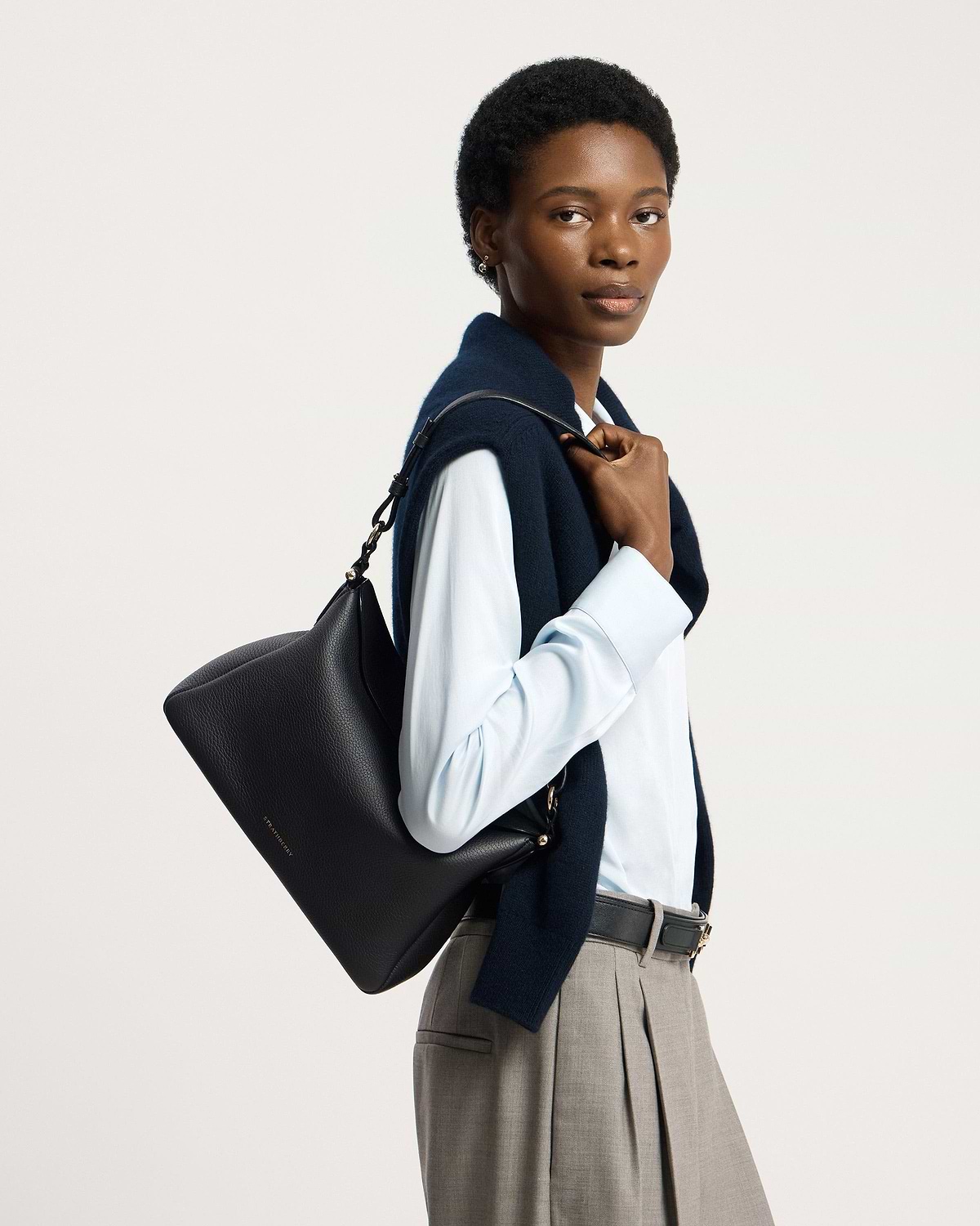 Model carrying black Strathberry Sway Maxi shoulder bag, wearing blue shirt and navy sweater.