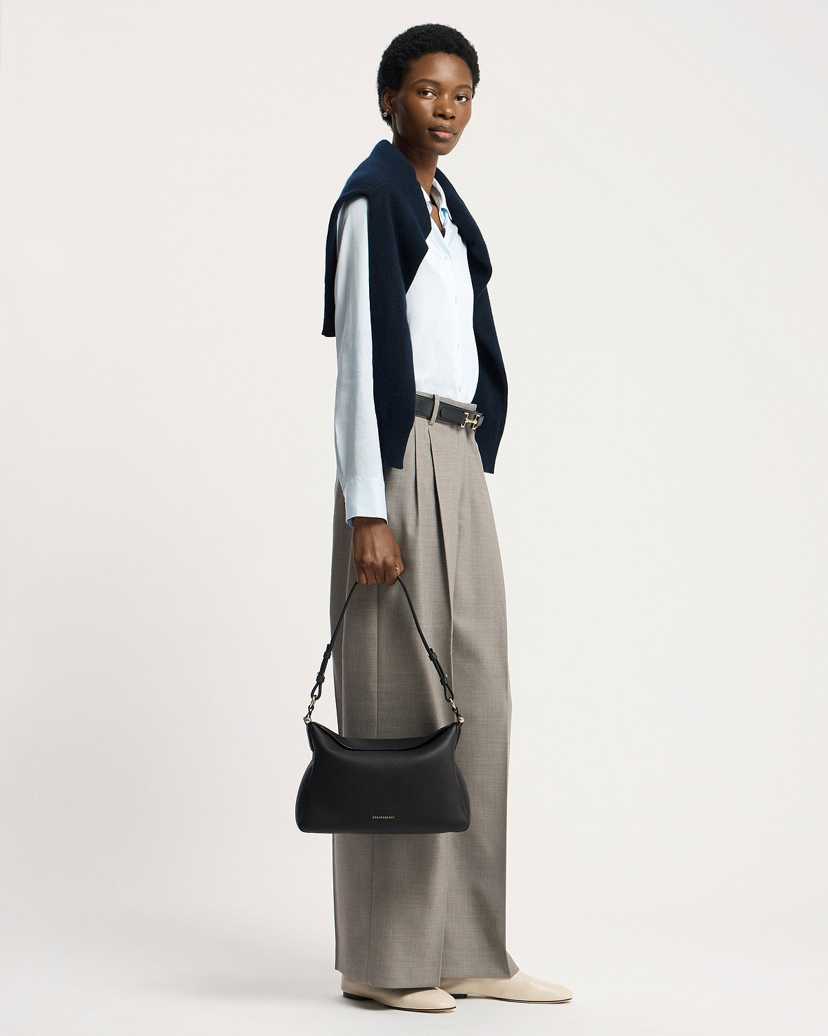 Model holding black Strathberry Sway Maxi handbag by its top handle.