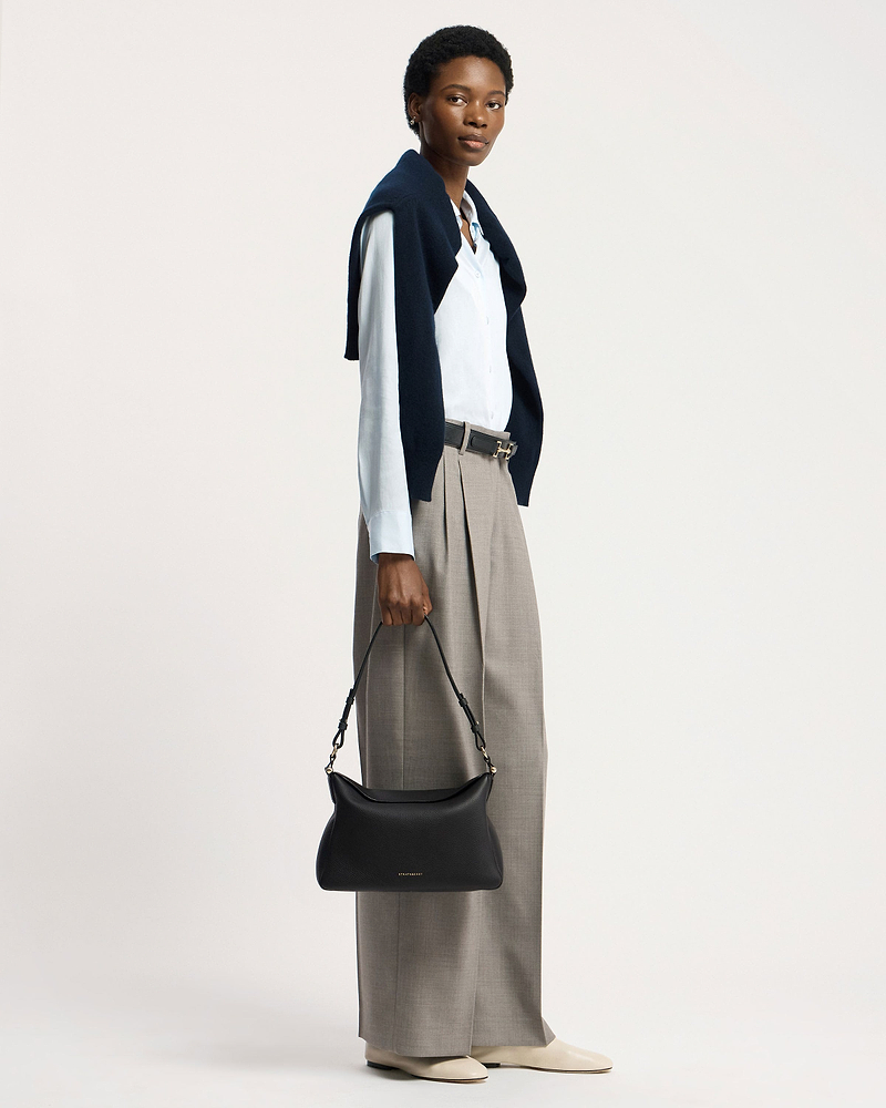 Model holding black Strathberry Sway Maxi handbag by its top handle.