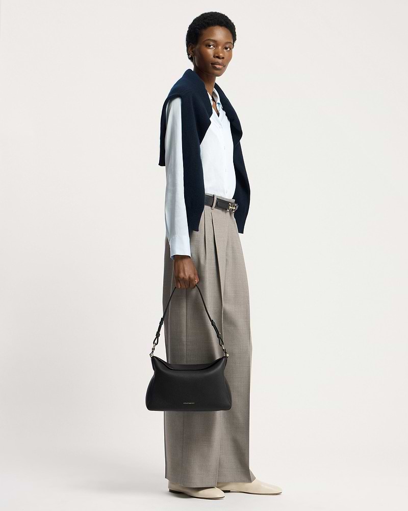Model holding black Strathberry Sway Maxi handbag by its top handle.