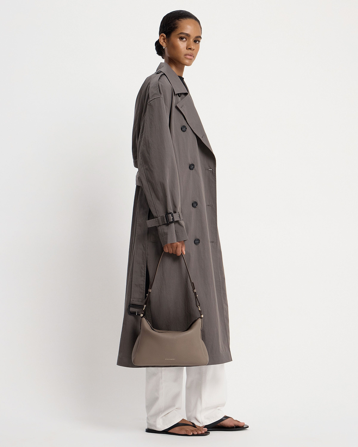 Model holding taupe Strathberry Sway Maxi shoulder bag against white background.