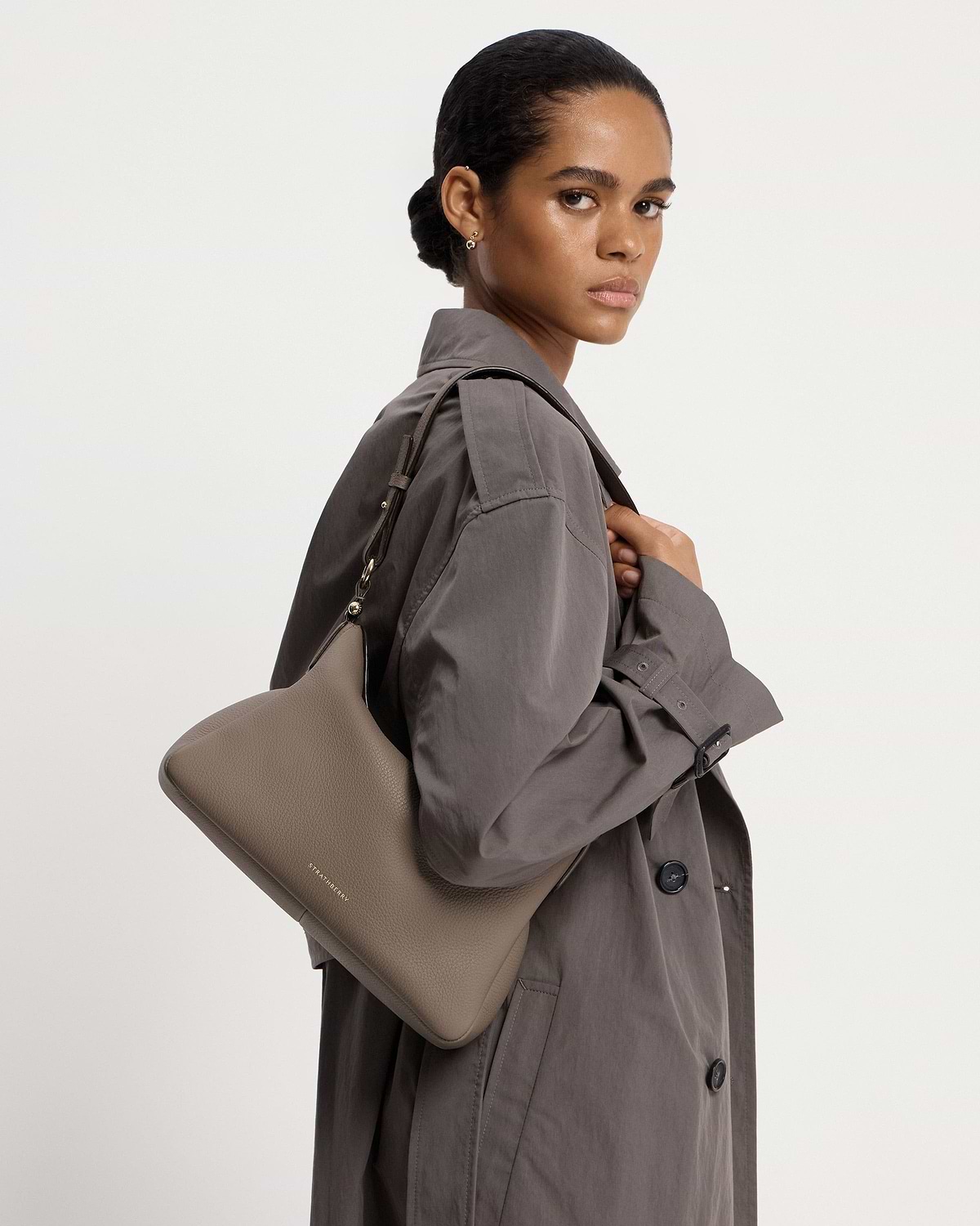 Model wearing grey coat carrying taupe Sway Maxi bag with Strathberry logo.