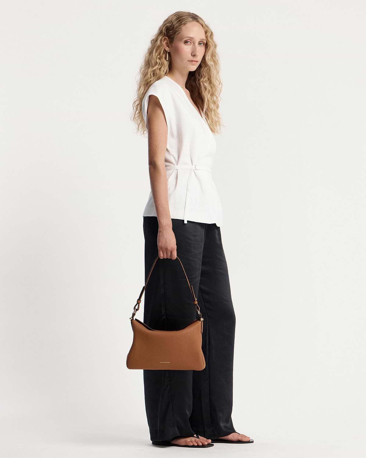 Model holding tan Sway Maxi shoulder bag with visible Strathberry wordmark.