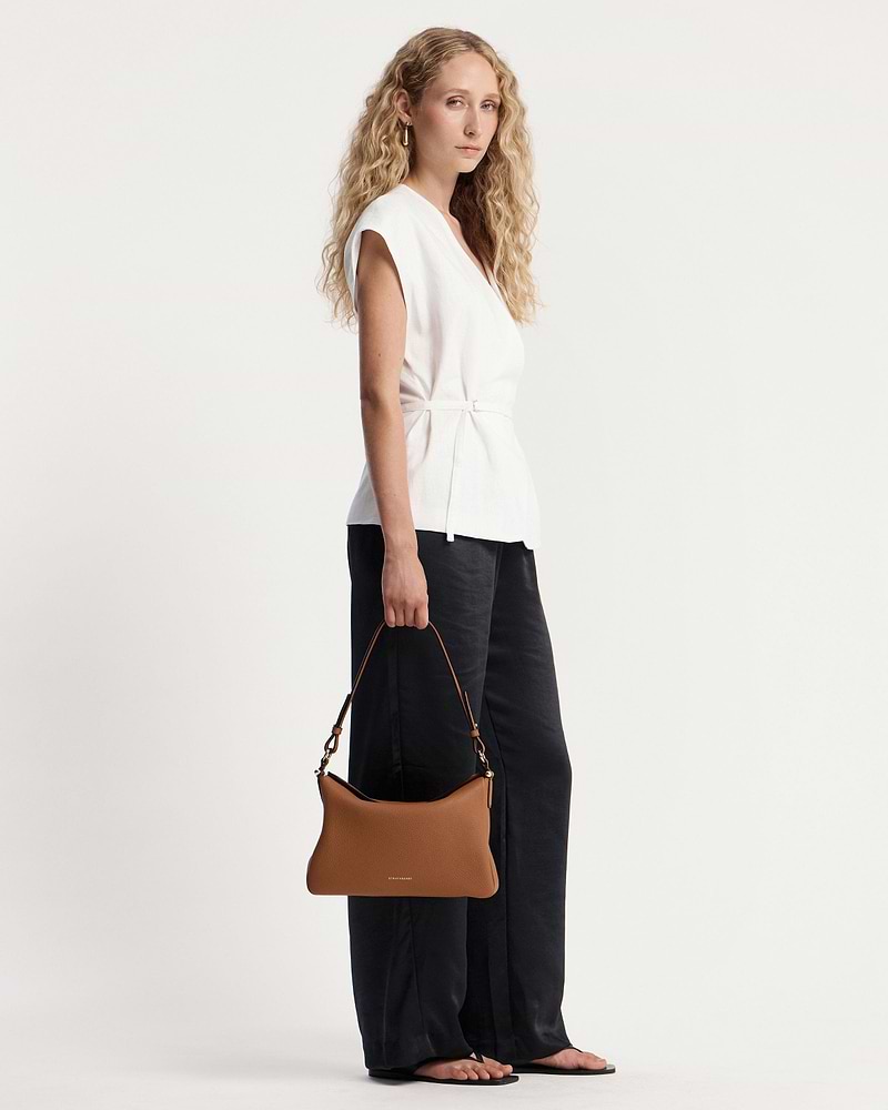 Model holding tan Sway Maxi shoulder bag with visible Strathberry wordmark.