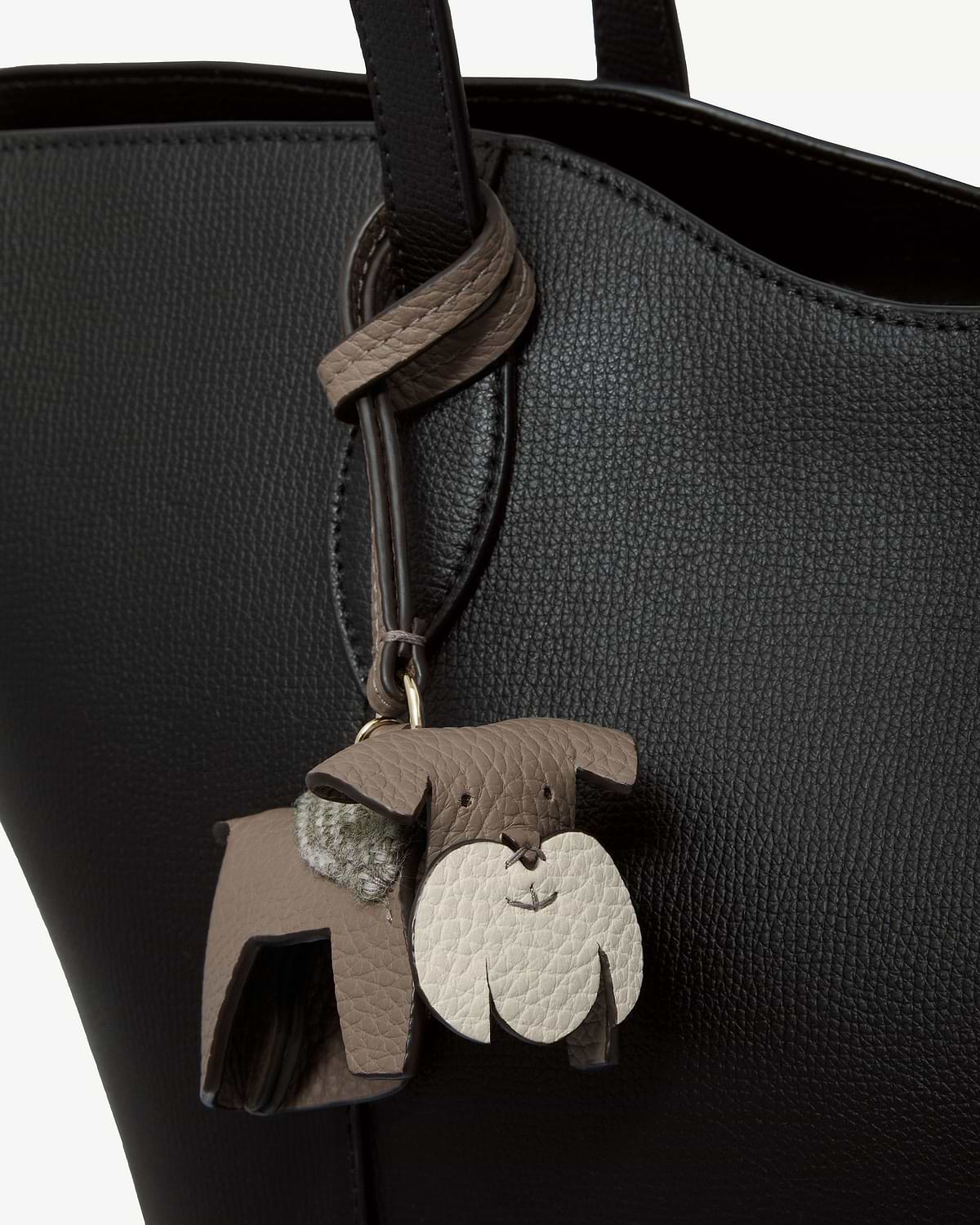 Taupe leather dog bag charm with cream face and tartan detail on black bag.