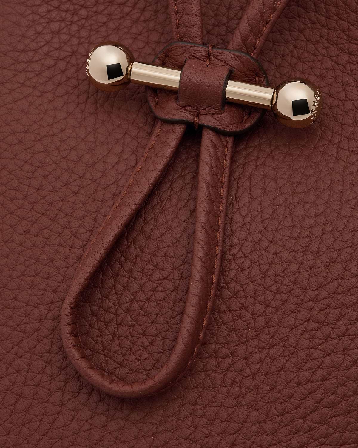 Pebbled walnut leather surface with drawstring cords and gold bar toggle fastener.