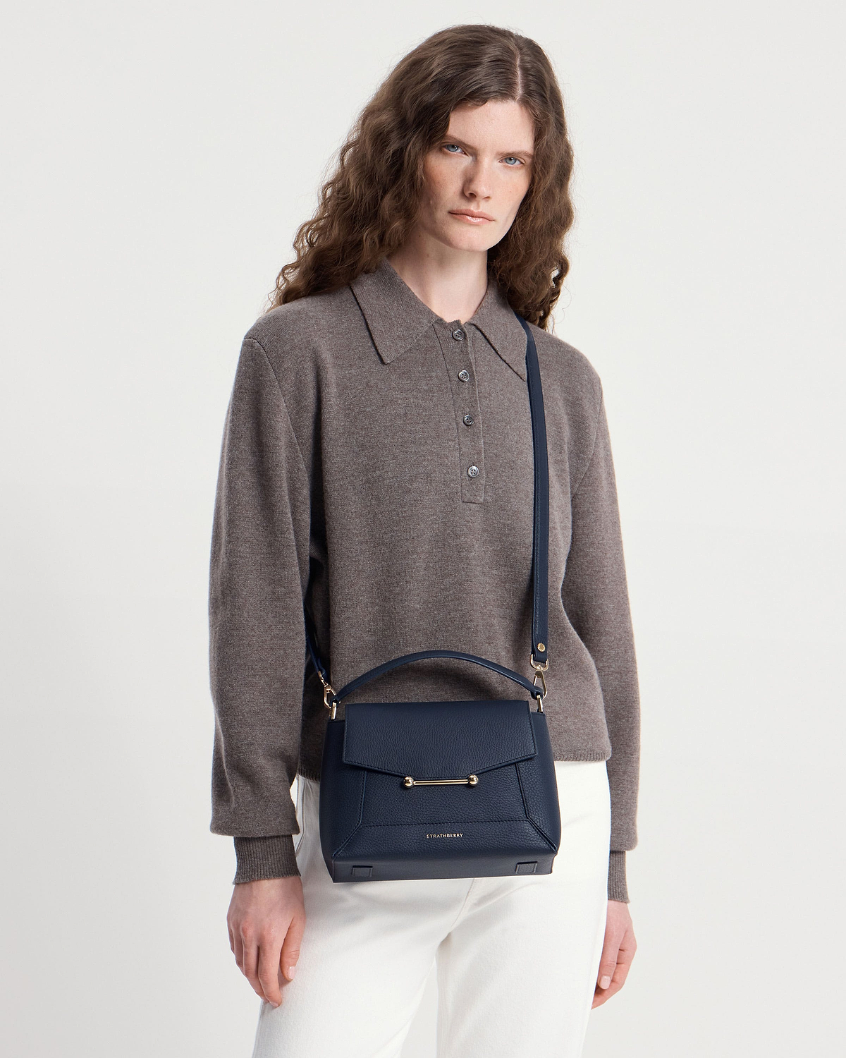 Model wearing navy Strathberry Mosaic bag crossbody with grey jumper and white trousers