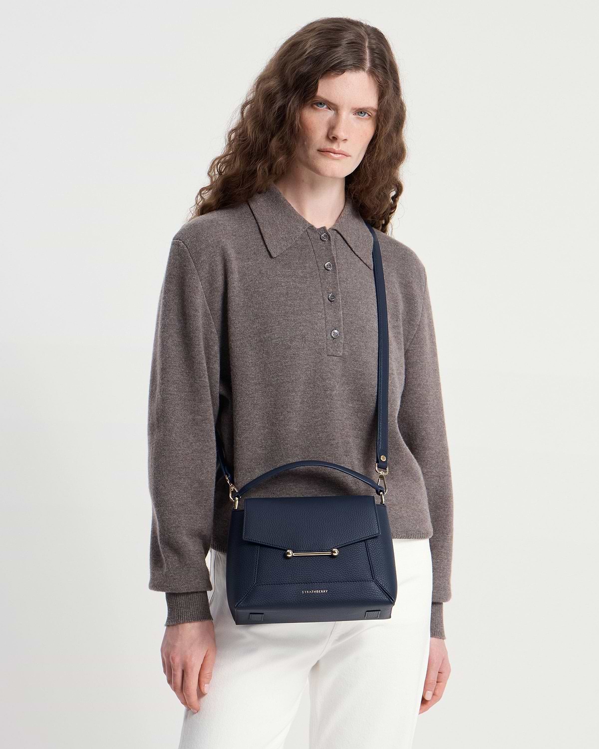 Model wearing navy Strathberry Mosaic bag crossbody with grey jumper and white trousers