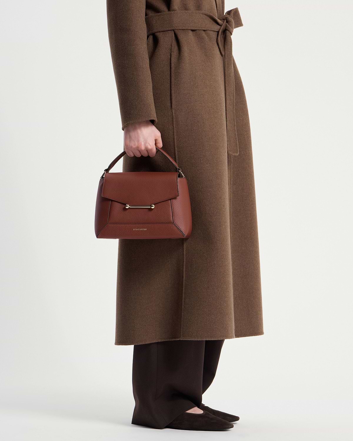 Model waist down holding a walnut mosaic bag with Strathberry logo.