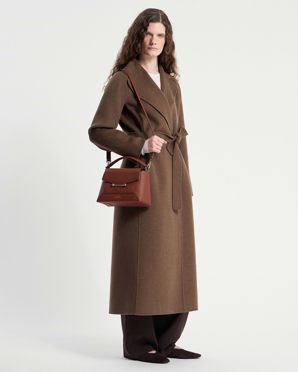 Model wearing brown coat carrying walnut mosaic bag with top handle and strap.
