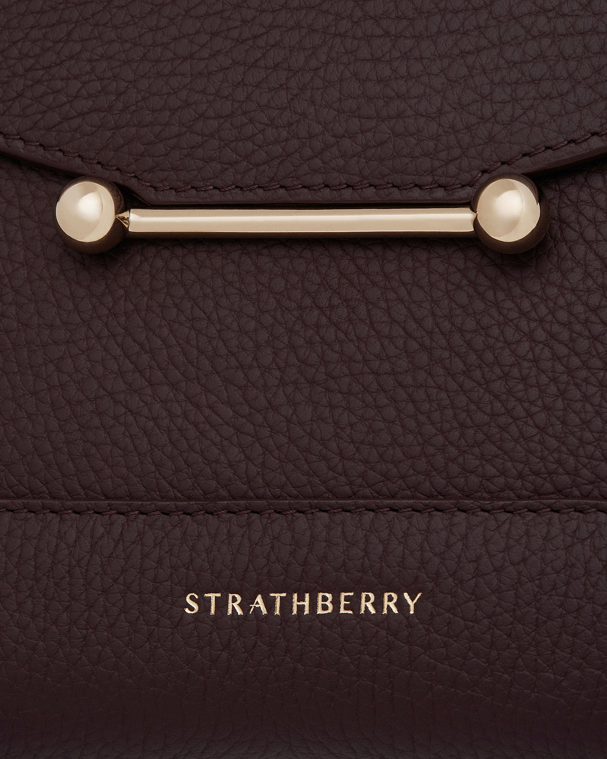 Close-up of burgundy pebbled leather mosaic bag with gold bar clasp, Strathberry logo.