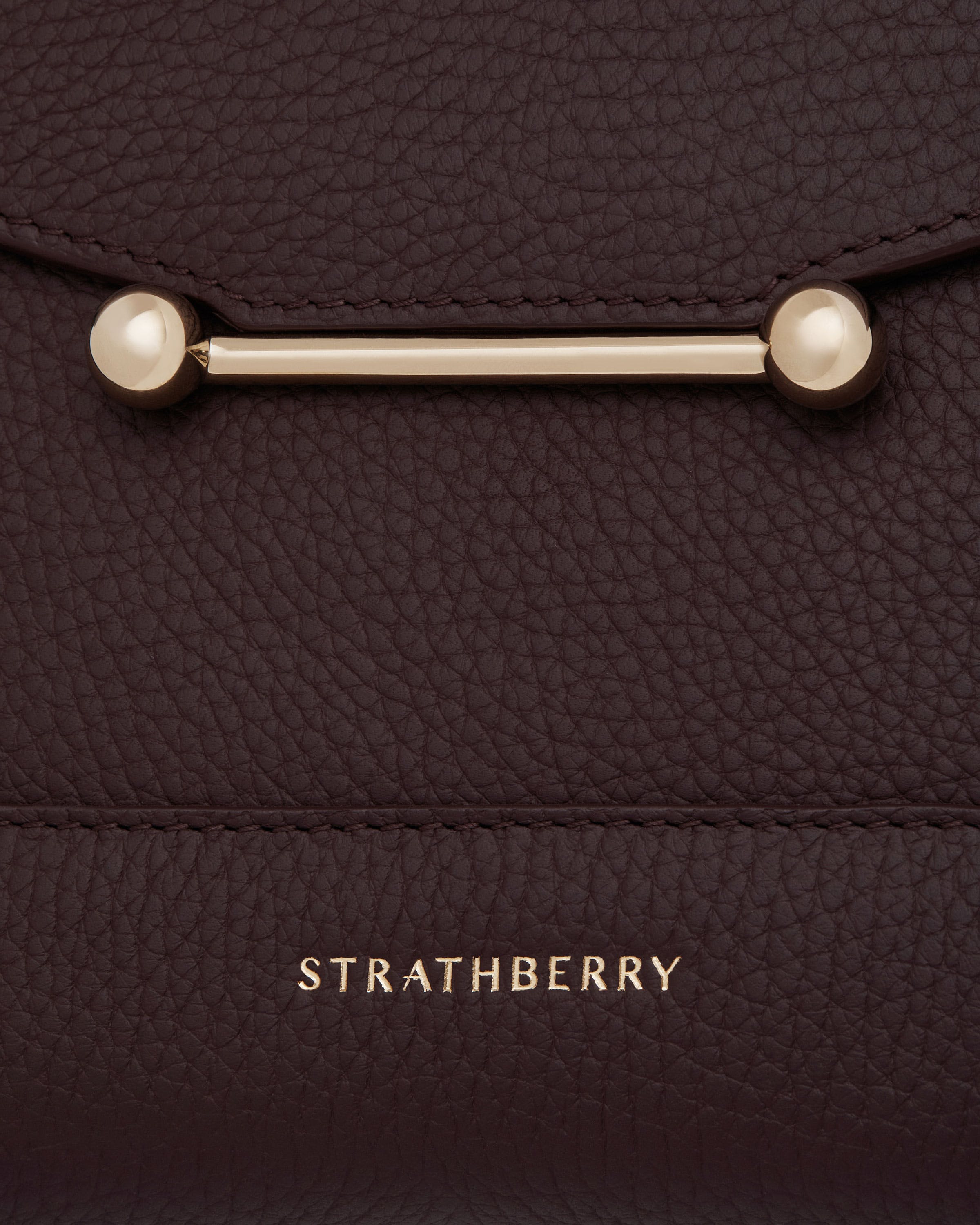 Close-up of burgundy pebbled leather mosaic bag with gold bar clasp, Strathberry logo.
