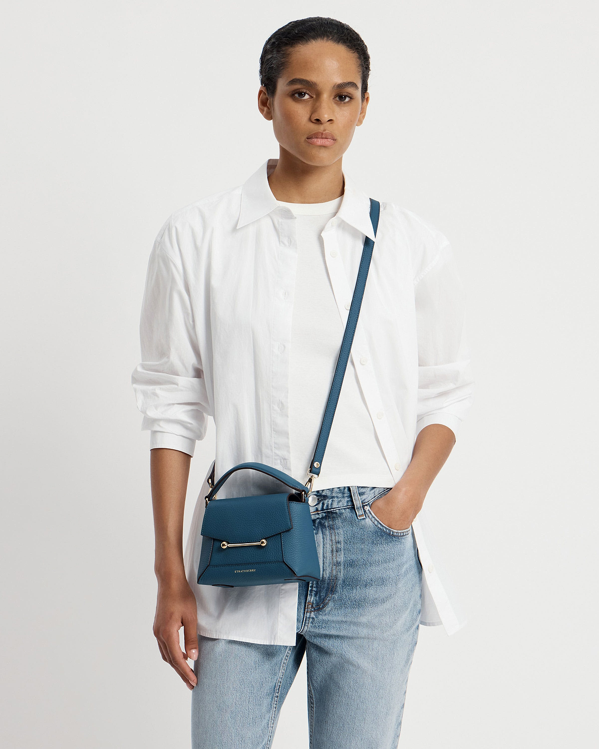 Model wearing white shirt and jeans carrying Strathberry Mosaic Nano bag in loch blue