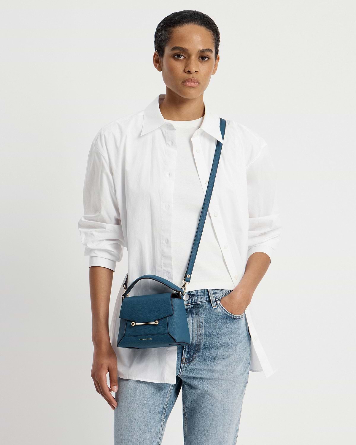 Model wearing white shirt and jeans carrying Strathberry Mosaic Nano bag in loch blue