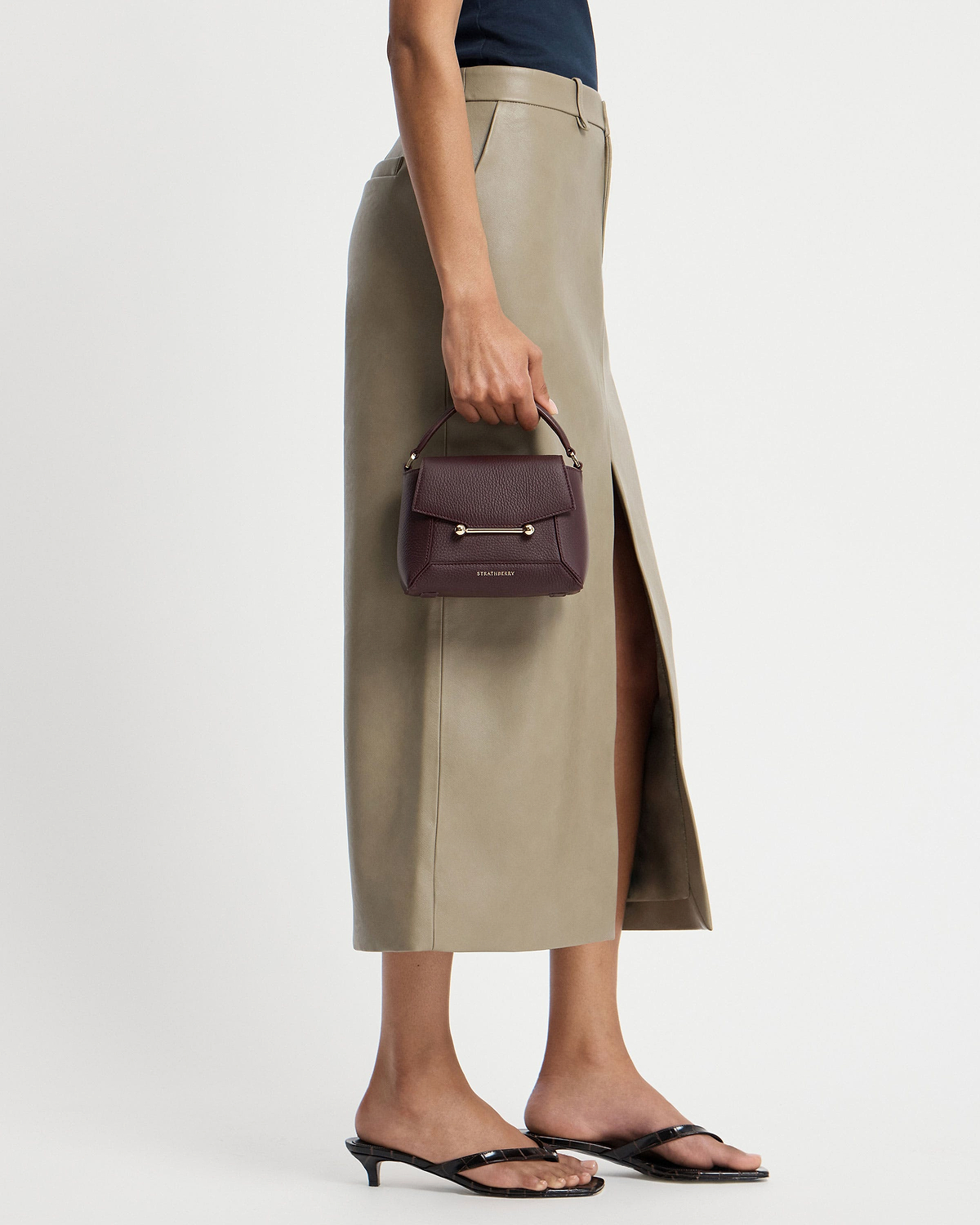 Strathberry Mosaic Nano burgundy top-handle bag held at model's side.