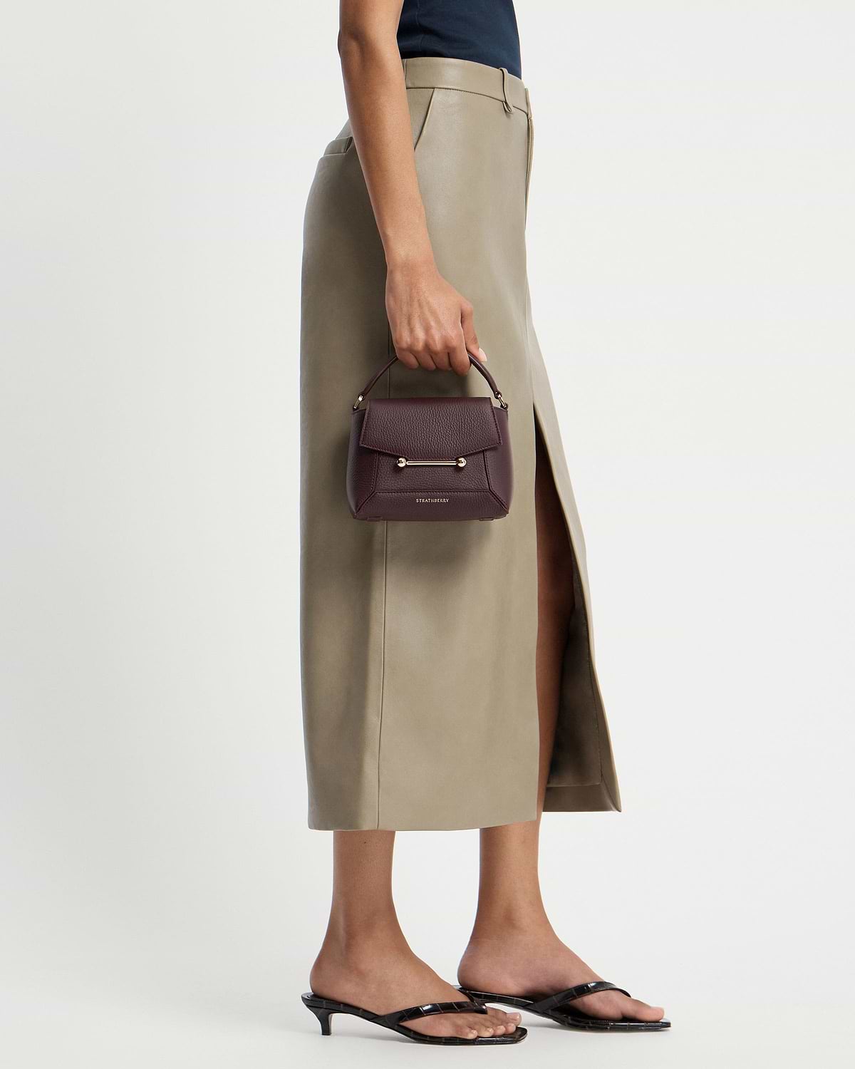 Strathberry Mosaic Nano burgundy top-handle bag held at model's side.