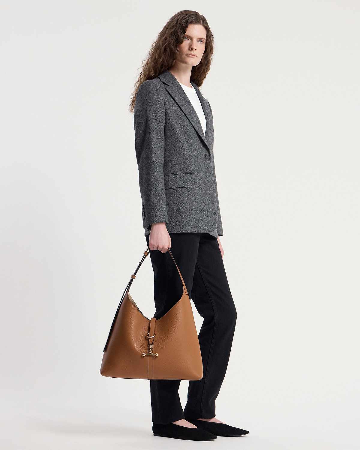 Model standing holding tan leather hobo bag with gold T-bar hardware.