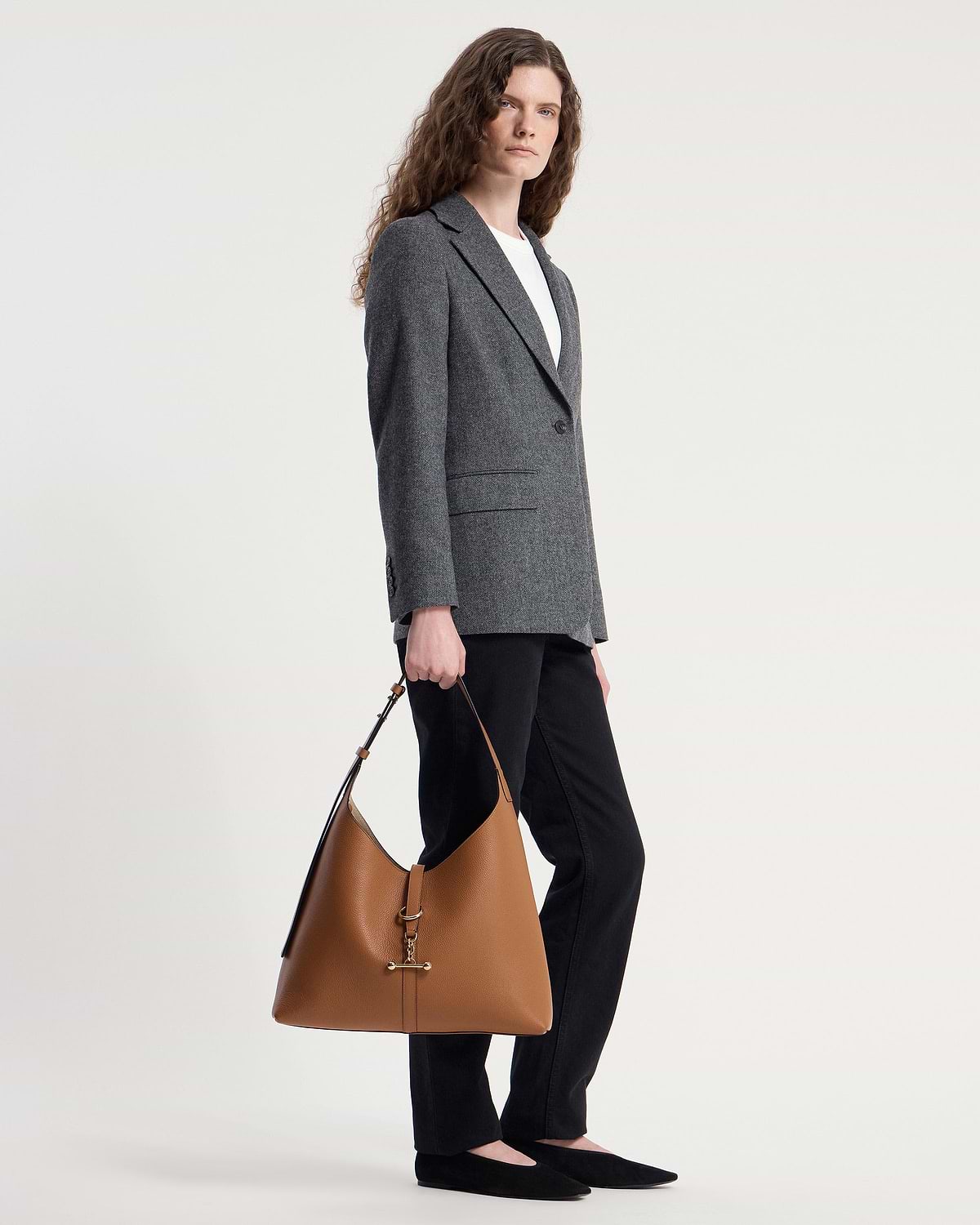 Model standing holding tan leather hobo bag with gold T-bar hardware.
