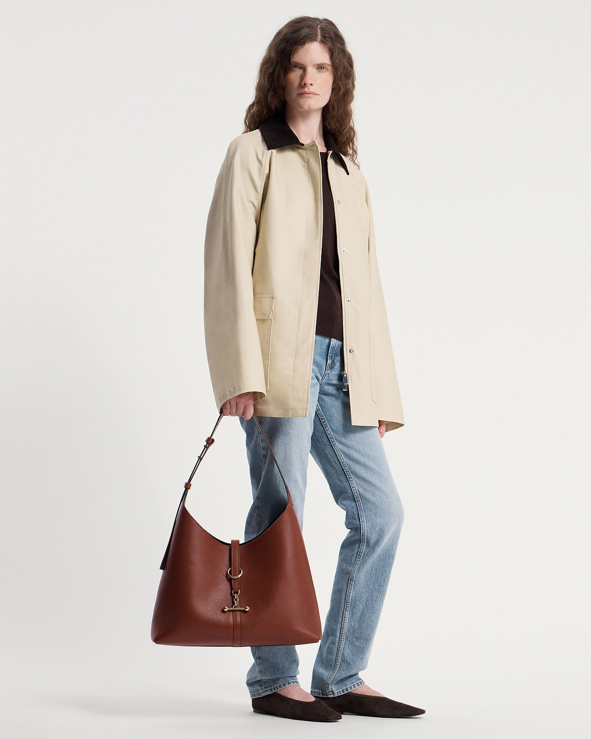 Model wearing a beige coat and jeans holding a walnut leather Kite Hobo Maxi bag.