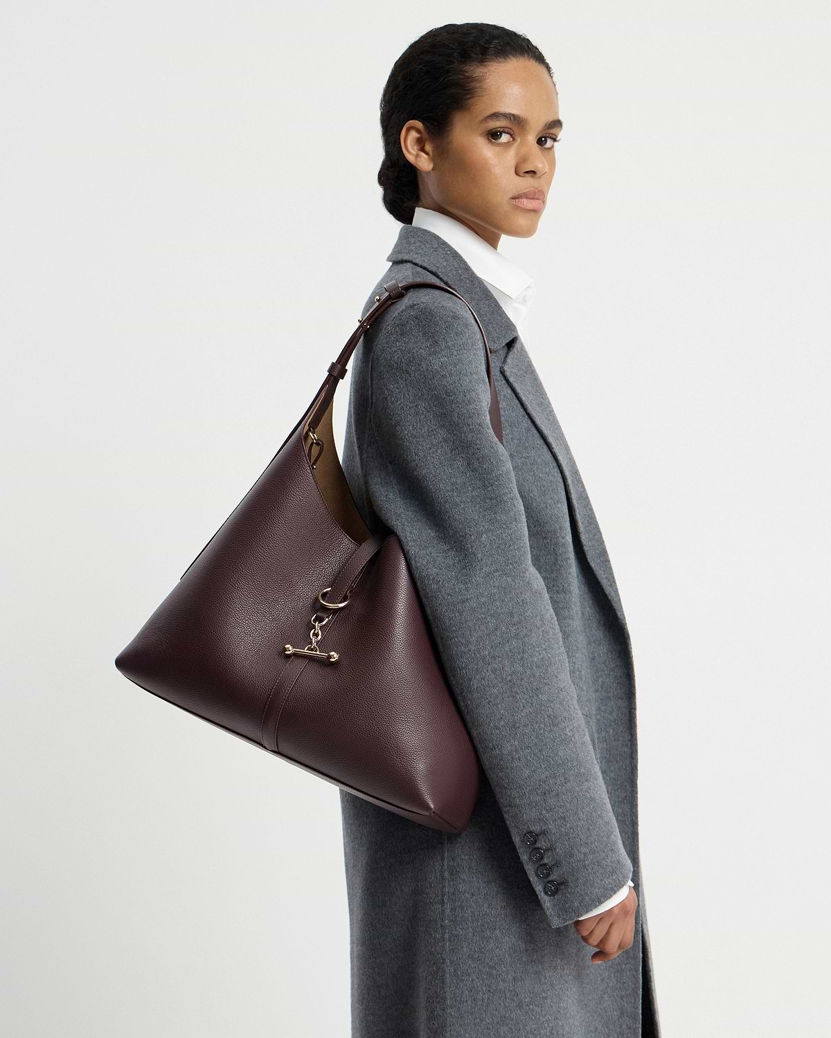 Model wearing a burgundy hobo shoulder bag over a grey coat.