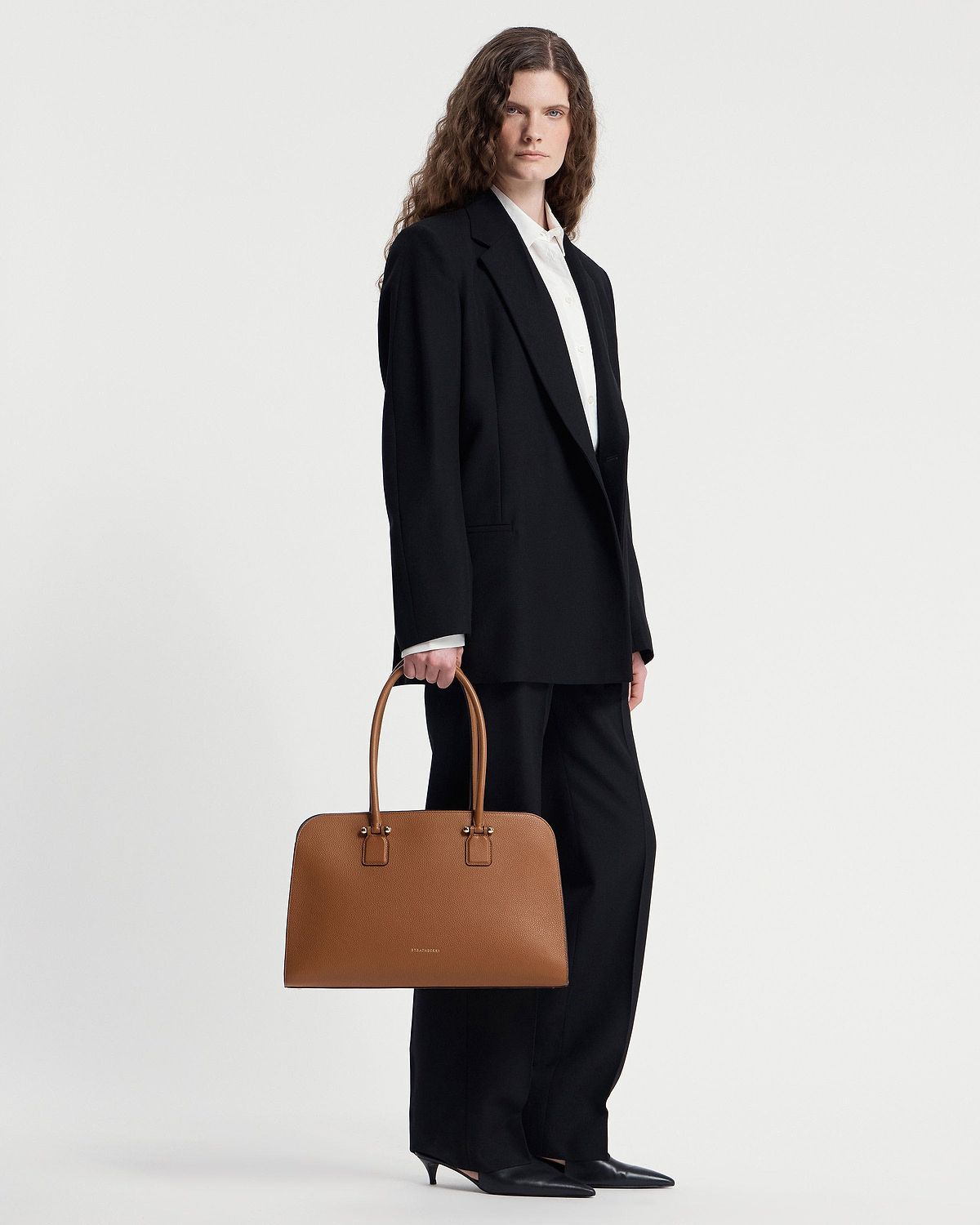 Model holding tan Georgia Maxi tote bag with Strathberry logo and double handles.