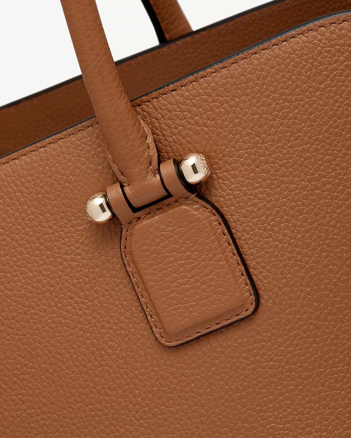 Tan pebbled leather bag showing handle attachment with gold studs.