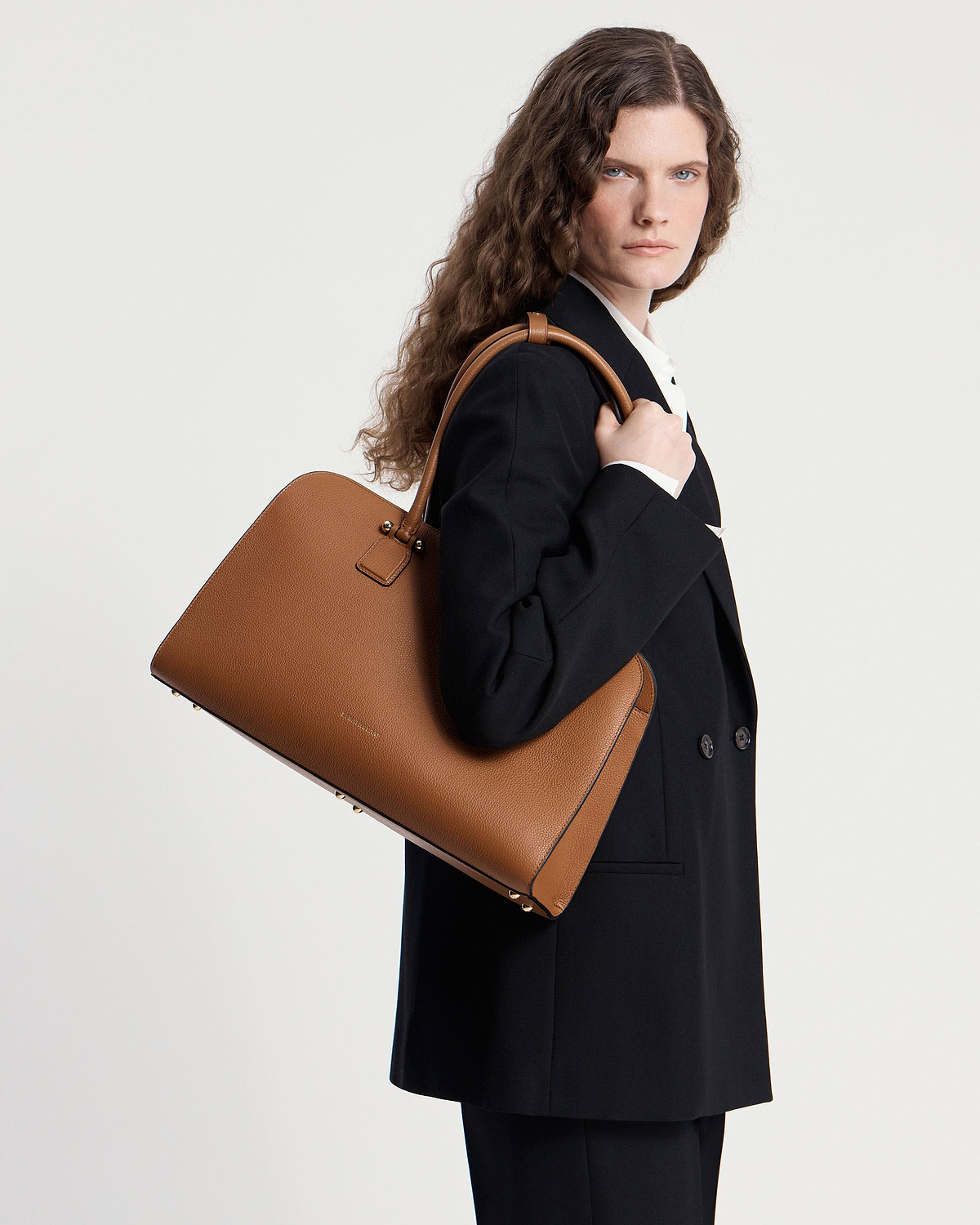 Model wearing black blazer carrying a tan leather tote bag over shoulder.
