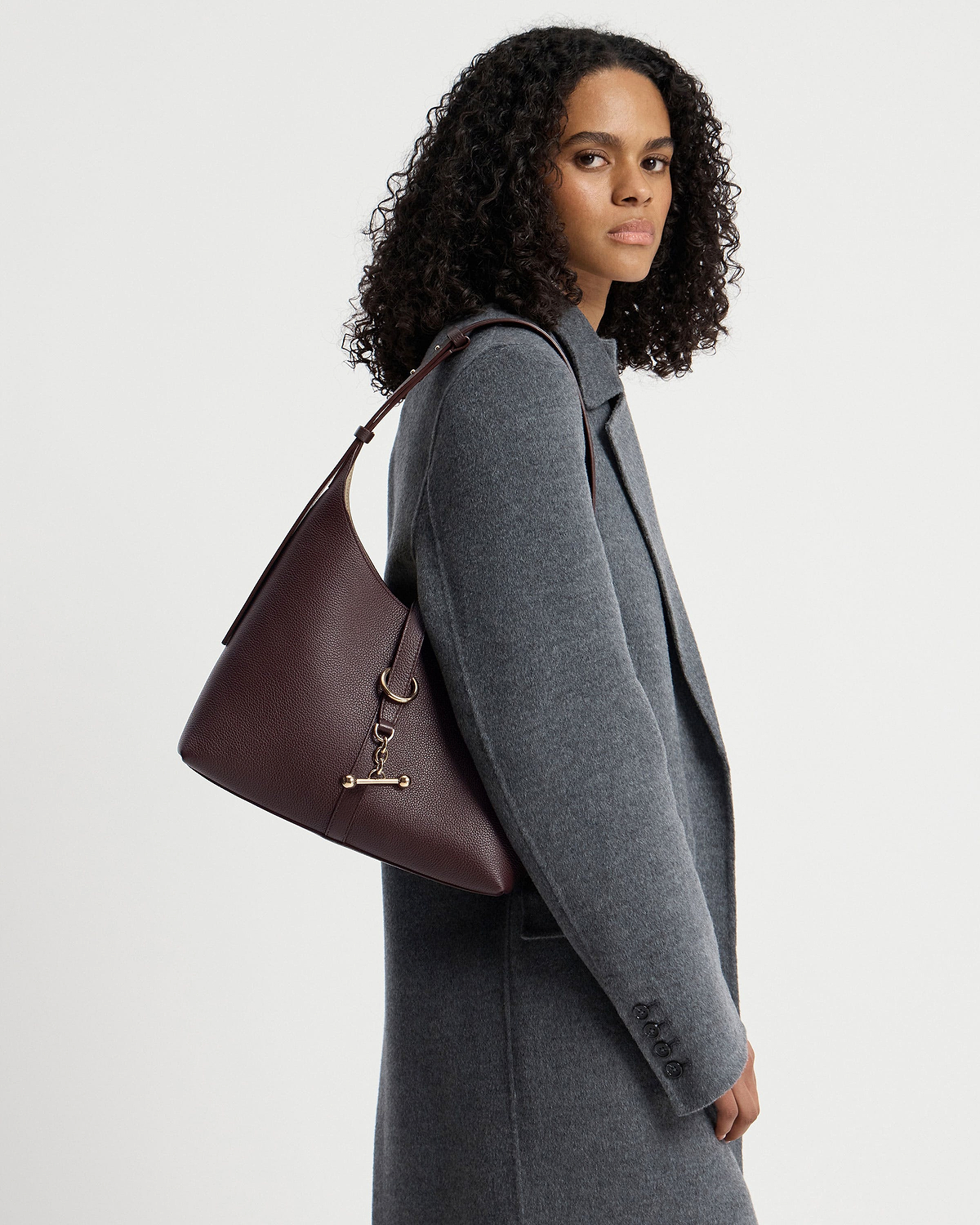 Woman wearing a grey coat carrying a burgundy hobo bag on her shoulder.