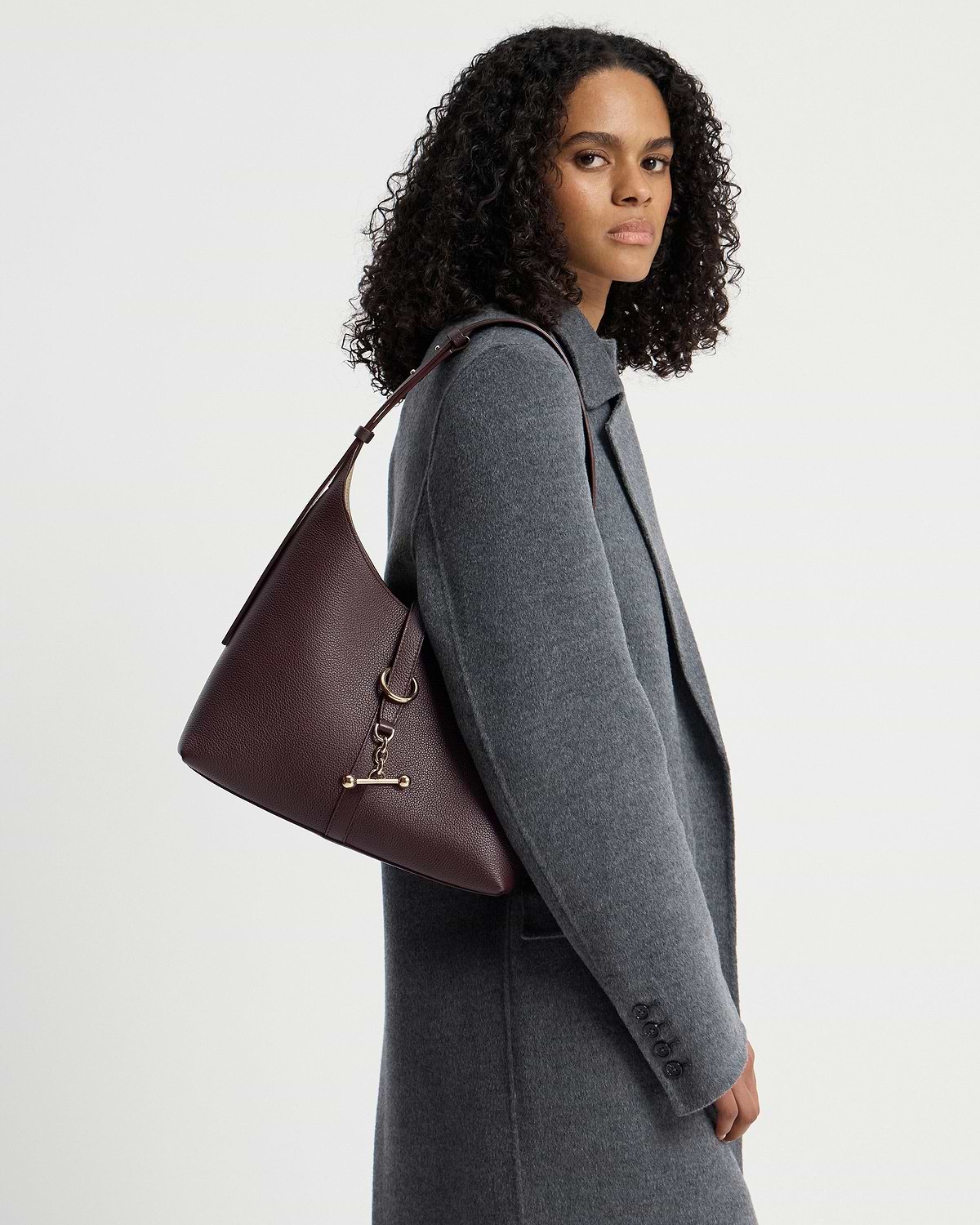 Woman wearing a grey coat carrying a burgundy hobo bag on her shoulder.