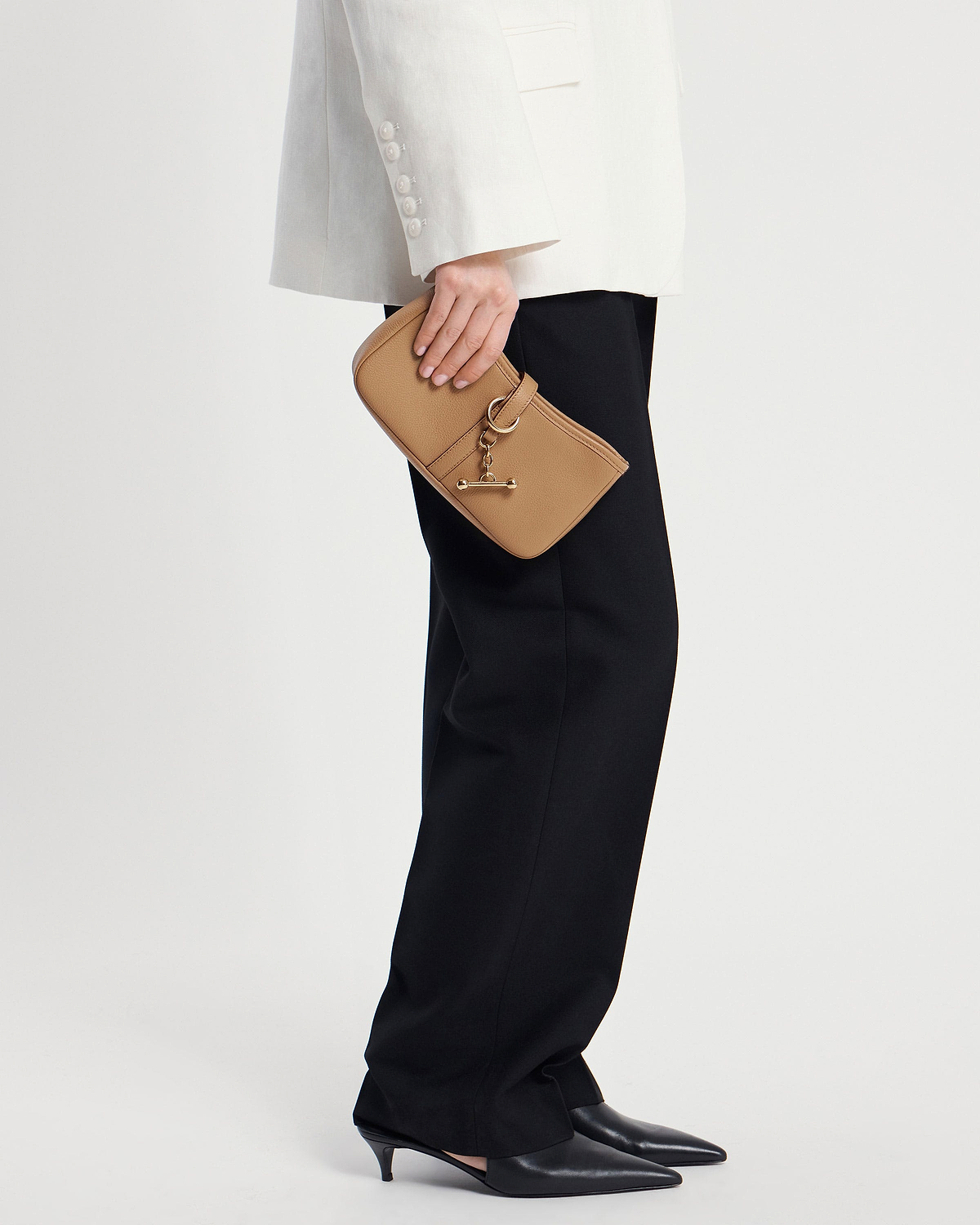 Model waist down holding a caramel leather clutch with gold chain and toggle detail.