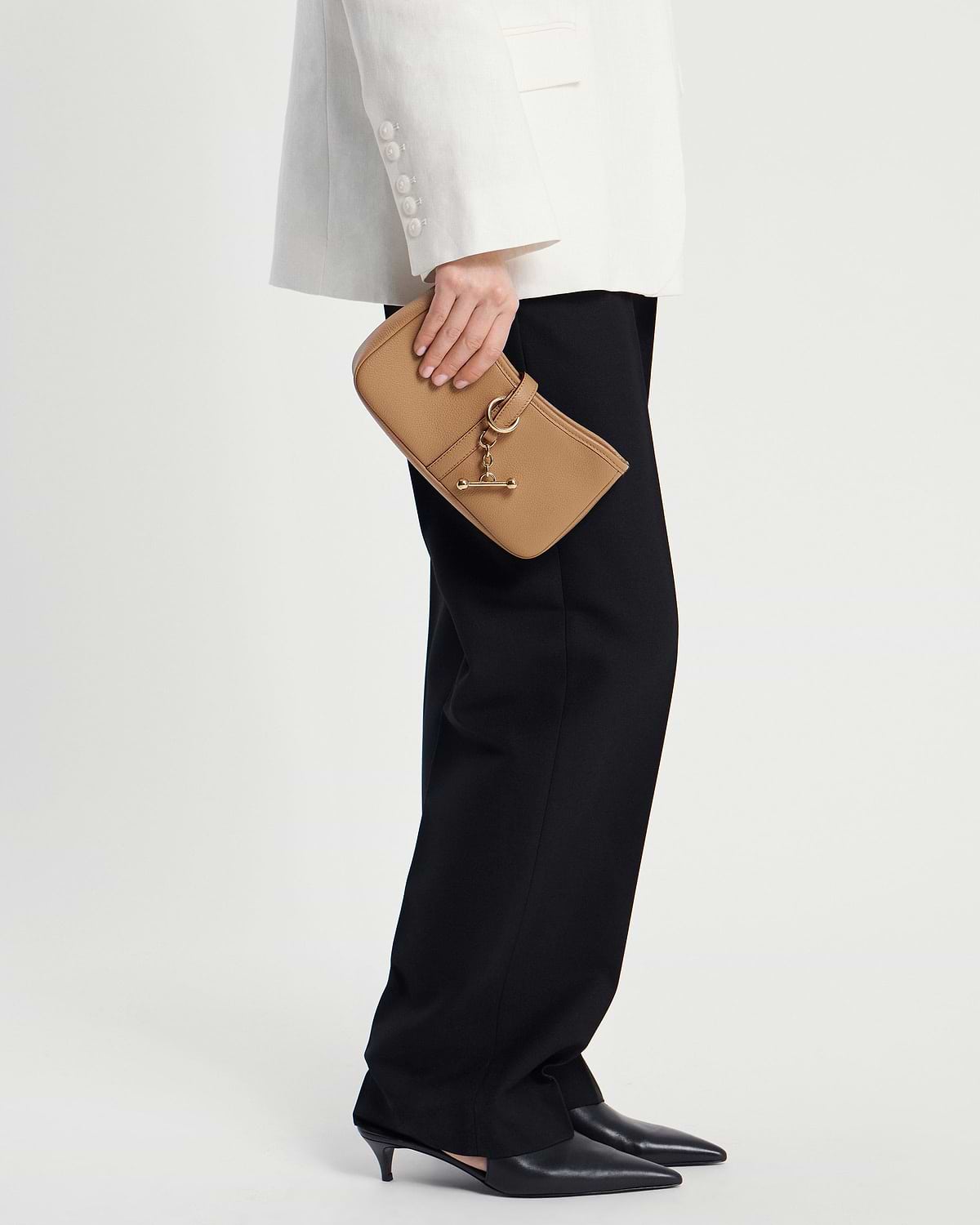 Model waist down holding a caramel leather clutch with gold chain and toggle detail.