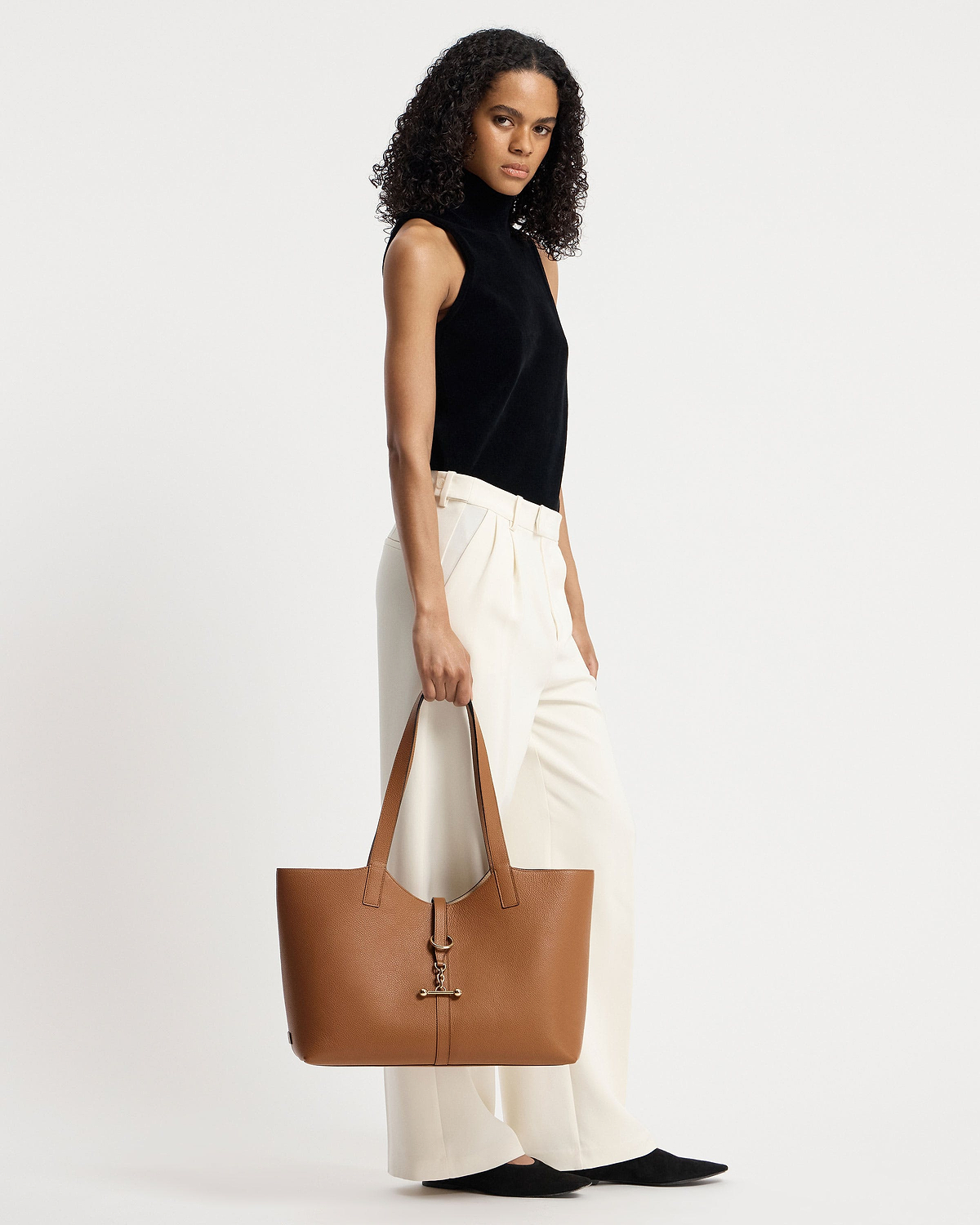 Model holding tan kite tote at her side, wearing black sleeveless top.