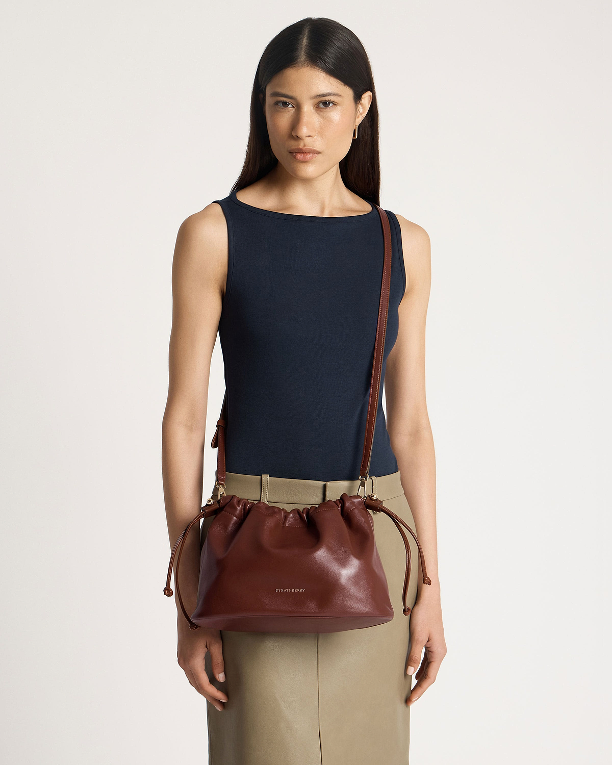 Model wearing navy sleeveless top and khaki skirt with Strathberry walnut drawstring bag