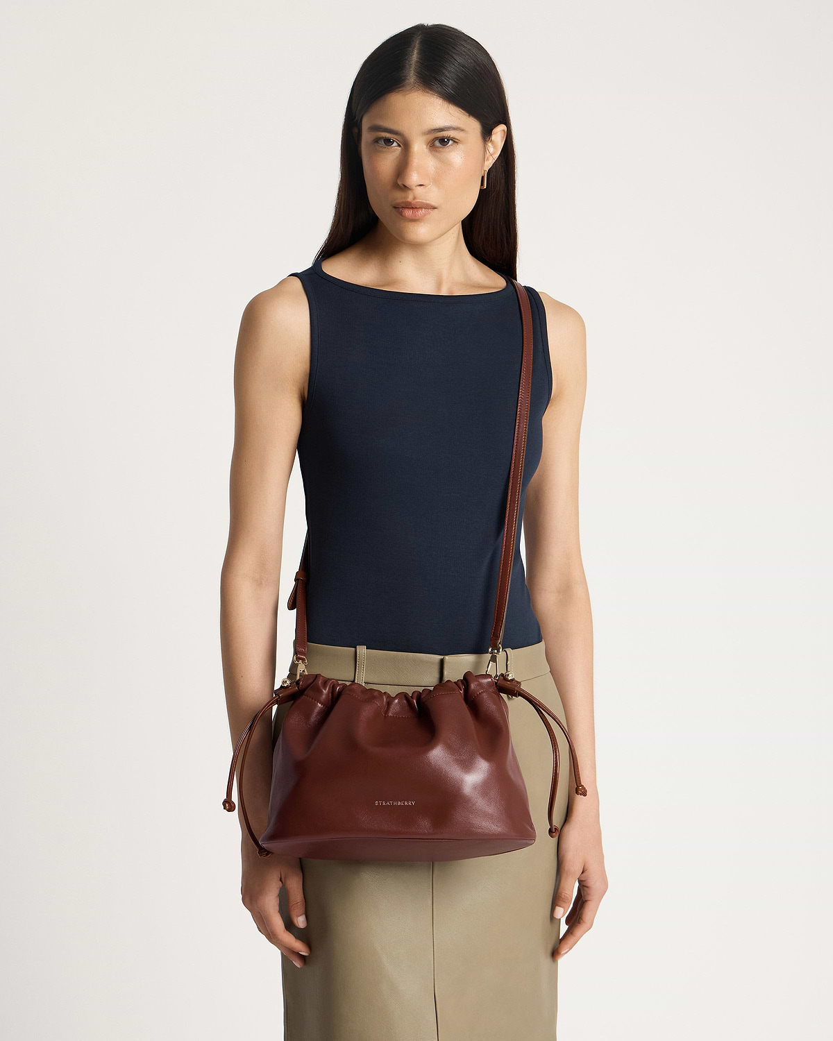 Model wearing navy sleeveless top and khaki skirt with Strathberry walnut drawstring bag