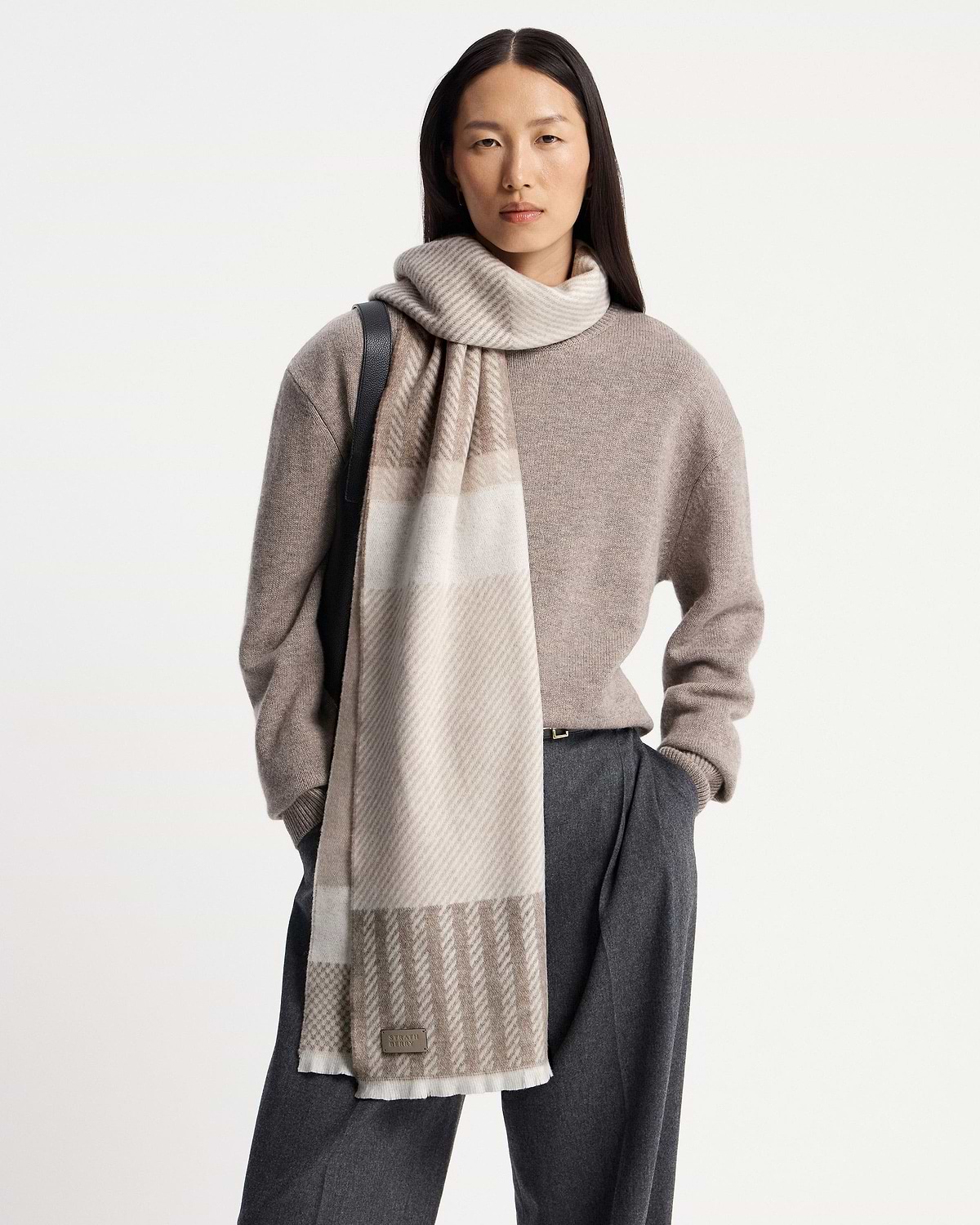 Model wearing taupe tartan cashmere scarf draped over shoulder, visible Strathberry logo.