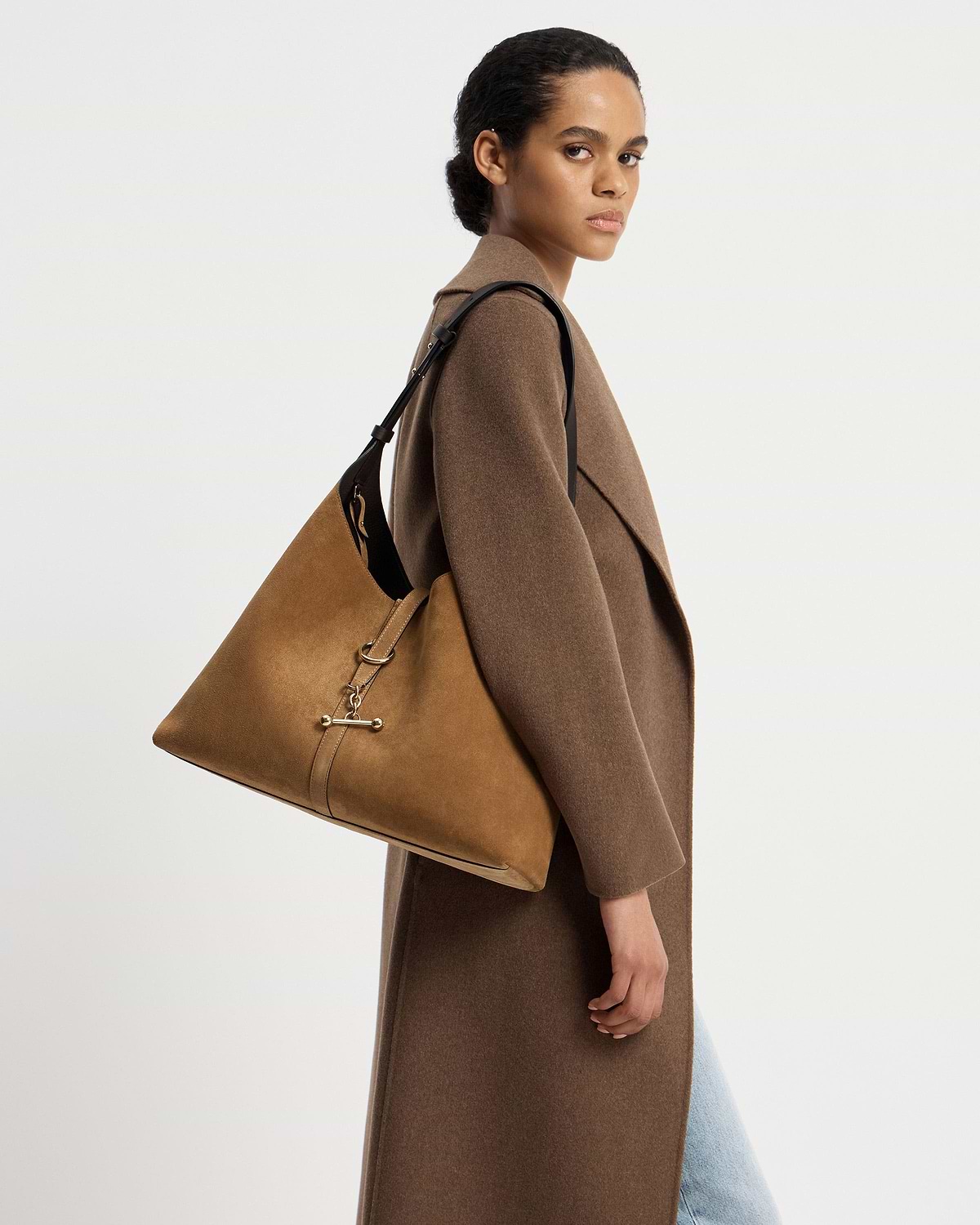 Model wearing brown coat carrying toffee suede hobo bag with espresso strap.