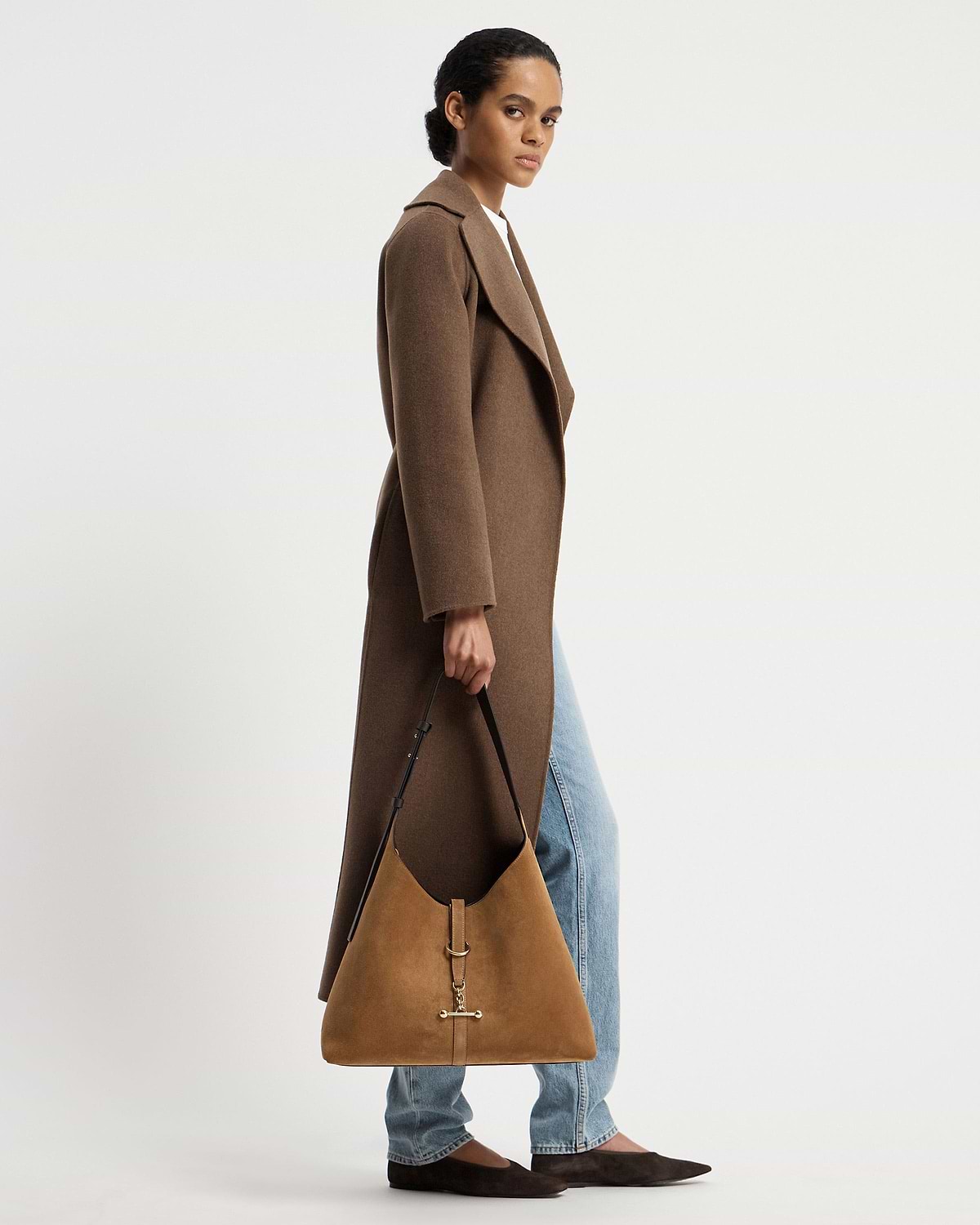Model wearing long brown coat holding a toffee suede hobo bag with espresso strap.
