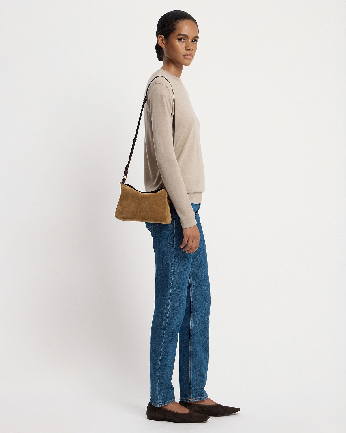 Woman wearing toffee suede shoulder bag with espresso strap, beige top and jeans.